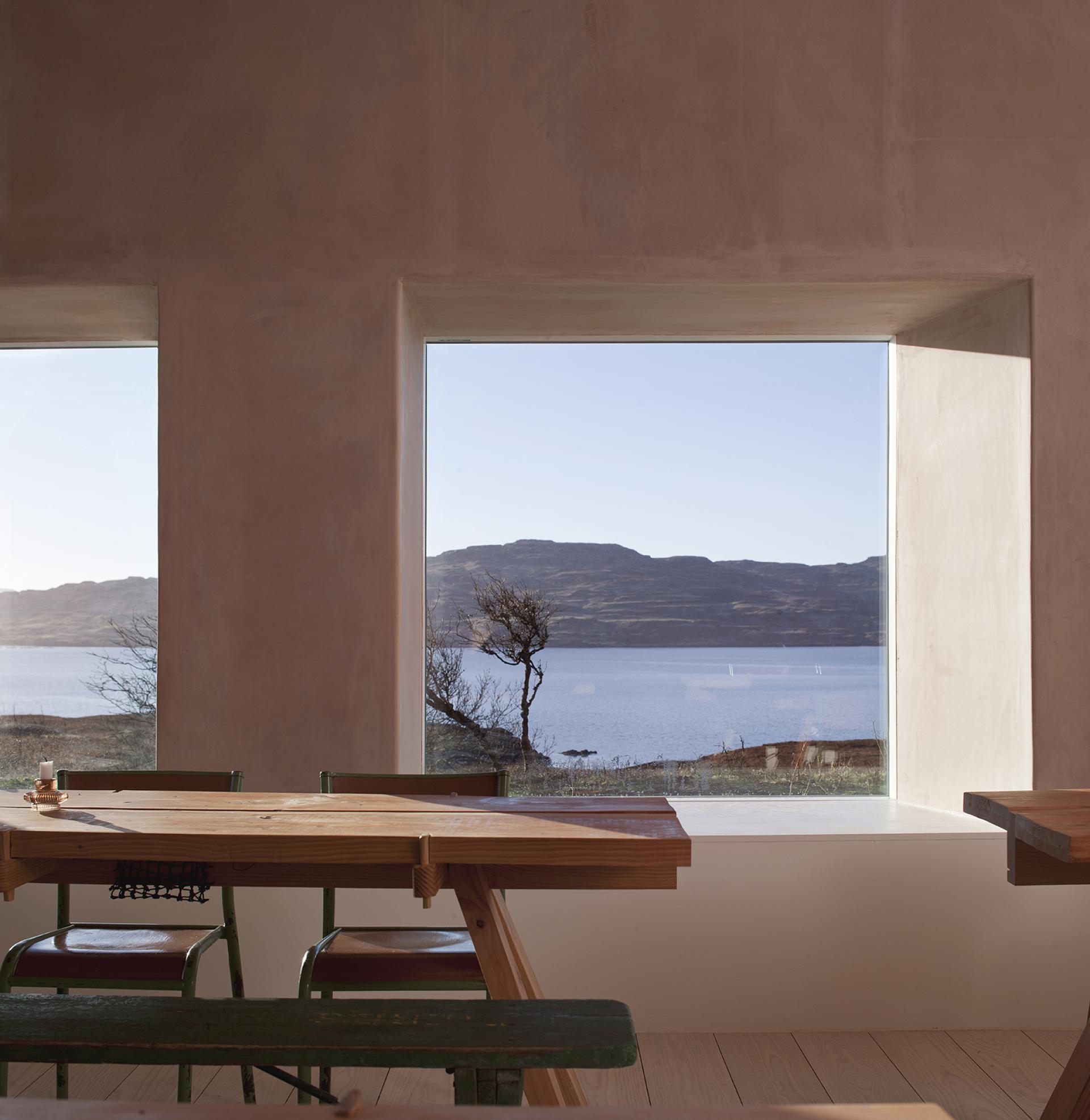 Modern interior featuring sustainable wooden furniture with large windows showcasing a serene lakeside view and mountains.