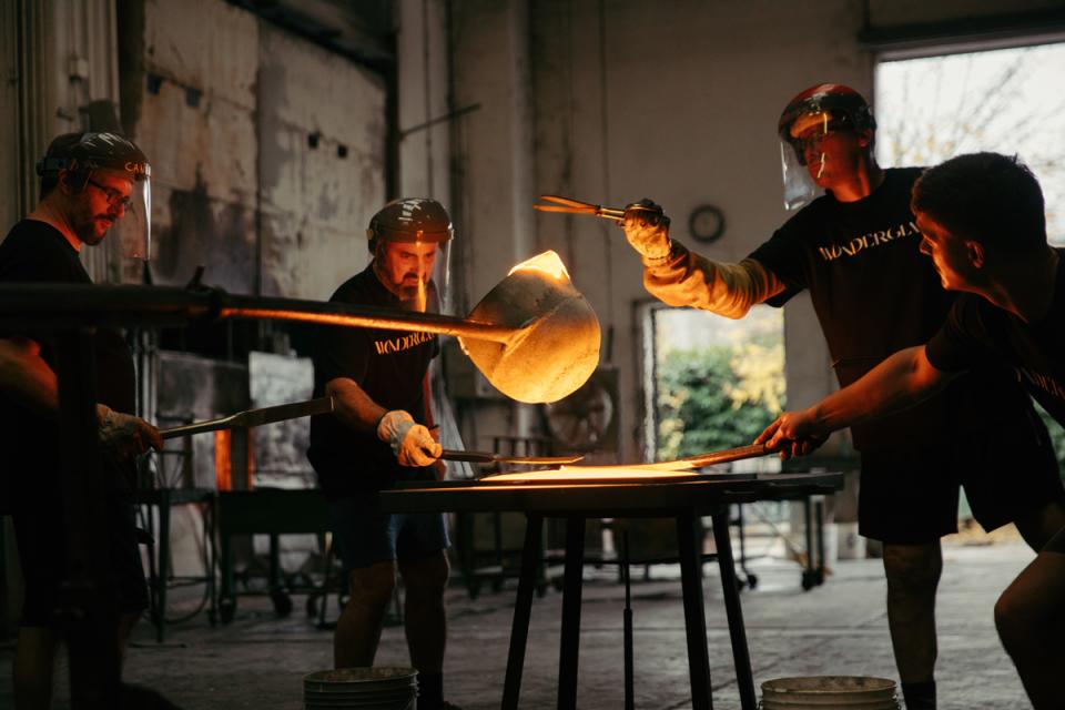 Craftsmen working collaboratively to pour molten glass into a mold for Melt, a unique cast glass furniture collection.