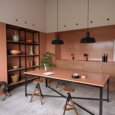 Modern kitchen with a coral accent wall, minimalist furniture, and decorative items, highlighting innovative design for Material Source Studio.