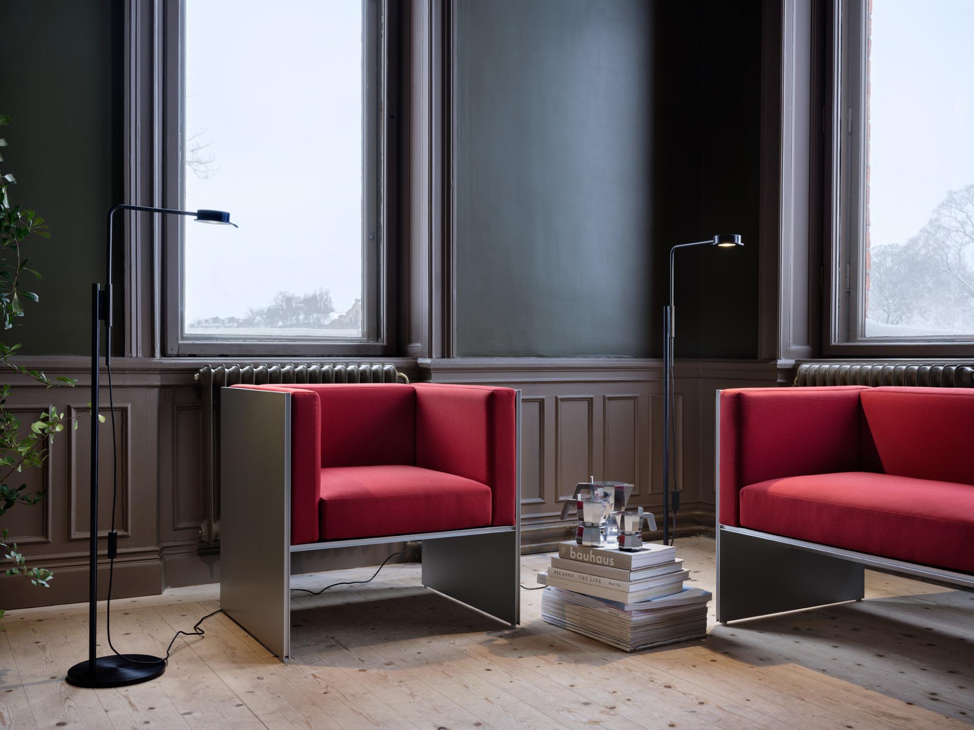 Stylish red armchairs with a black w102 Chipperfield lamp and books on a table in a modern interior.