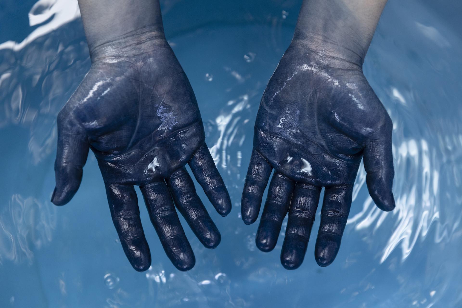 Hands stained with indigo dye above a blue water surface, showcasing traditional Japanese dyeing techniques and artistry.