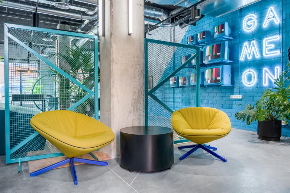 Vibrant co-working space at The Student Hotel Barcelona featuring stylish yellow chairs and a neon "Game On" sign.