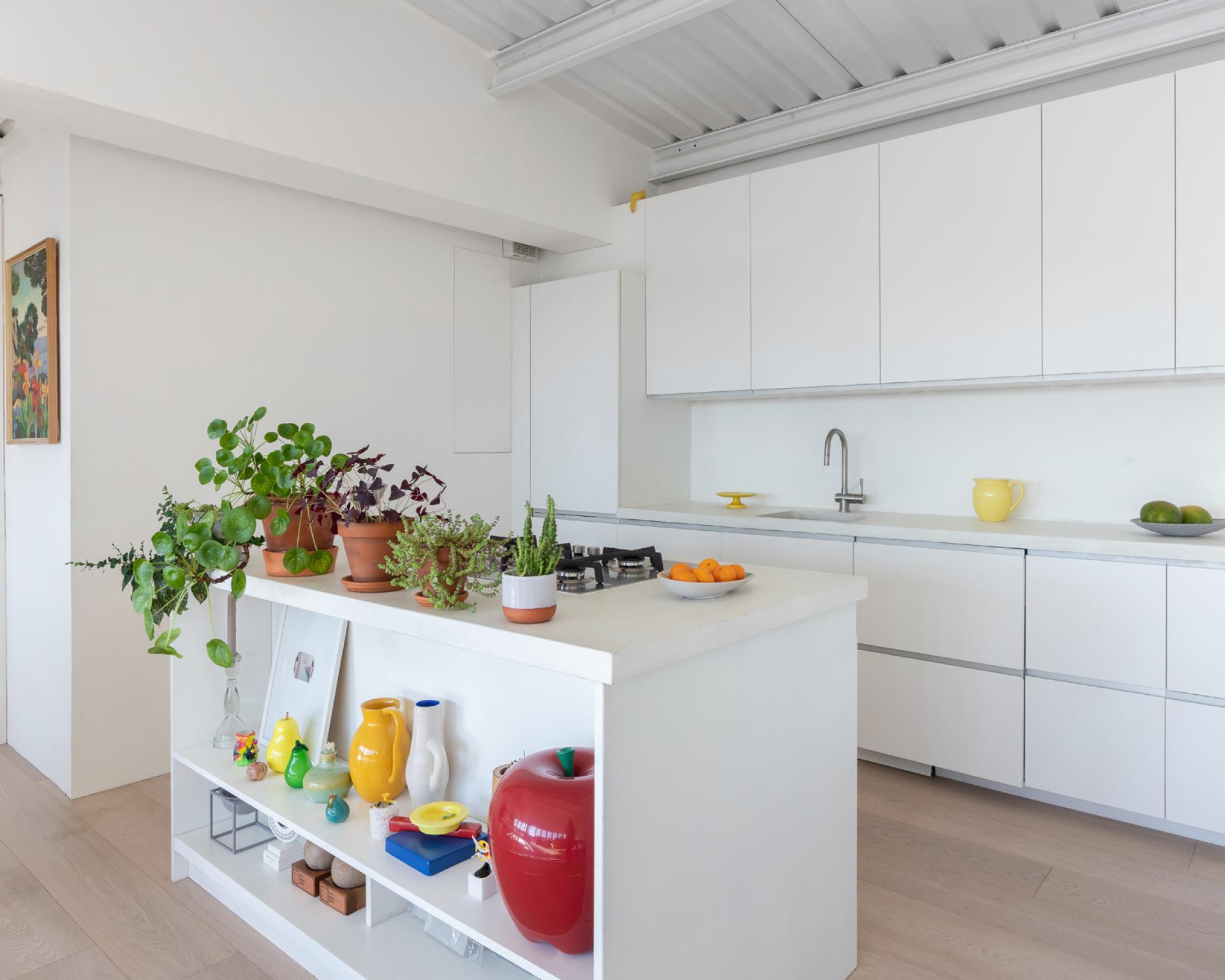 Modern kitchen in a studio flat, showcasing sleek white cabinetry, vibrant plants, and colorful decor elements.