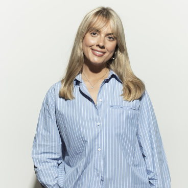 Rebecca Finney, creative director at Jasper Sanders + Partners, smiles confidently in a striped shirt against a light background.