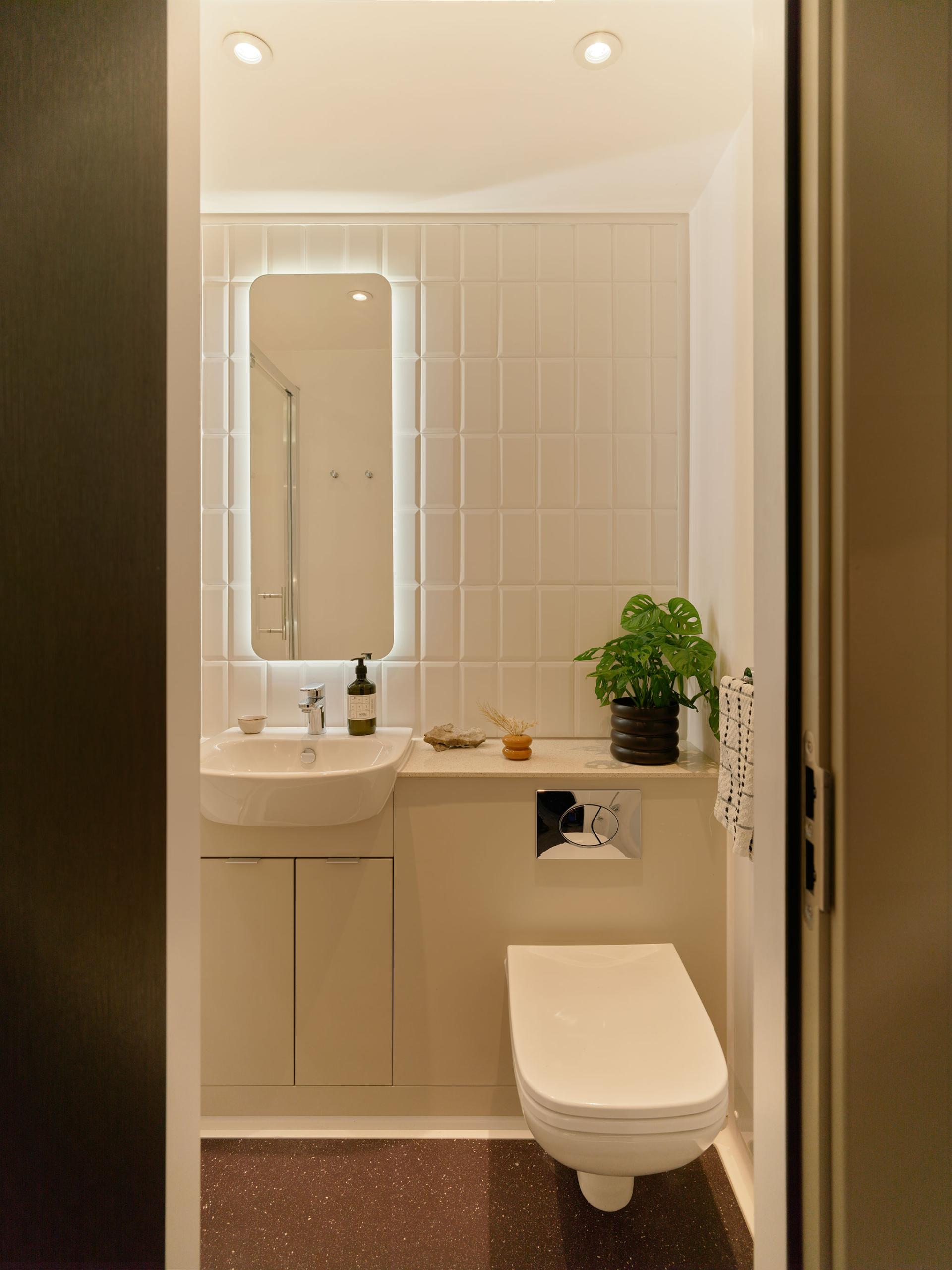 Modern bathroom design featuring a stylish toilet, sink, and decorative plant, highlighting the interior by Jasper Sanders + Partners.