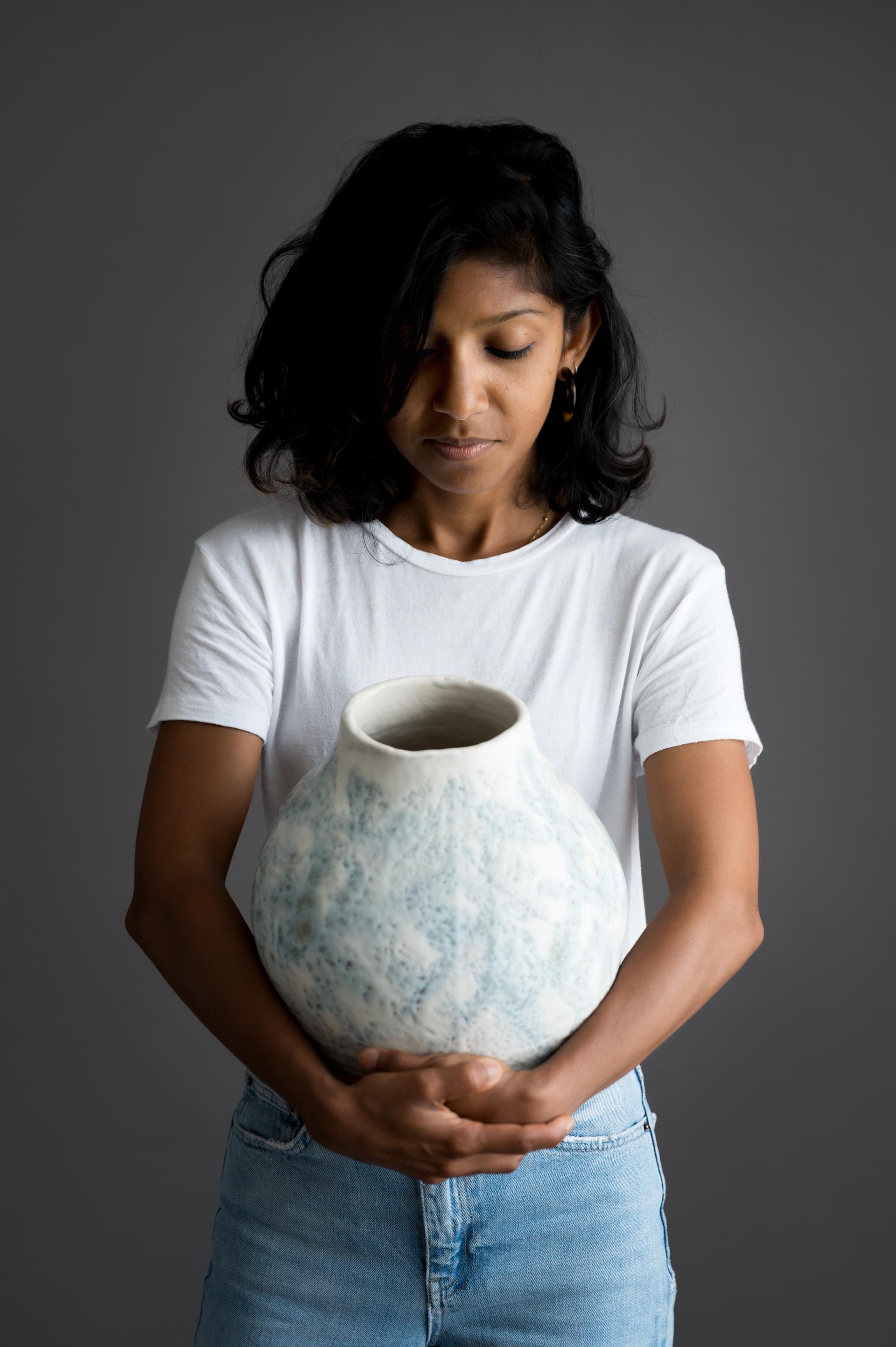 A woman in a white shirt holds a handcrafted ceramic vase, showcasing Bristol's vibrant craft community.
