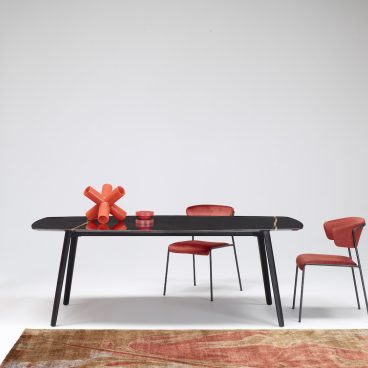 Elegant black table inspired by cuttlefish bone, paired with modern red chairs and decorative orange objects.