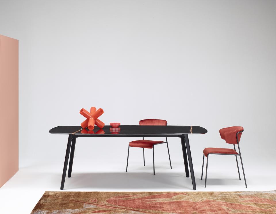 Elegant black table inspired by cuttlefish bone, paired with modern red chairs and decorative orange objects.
