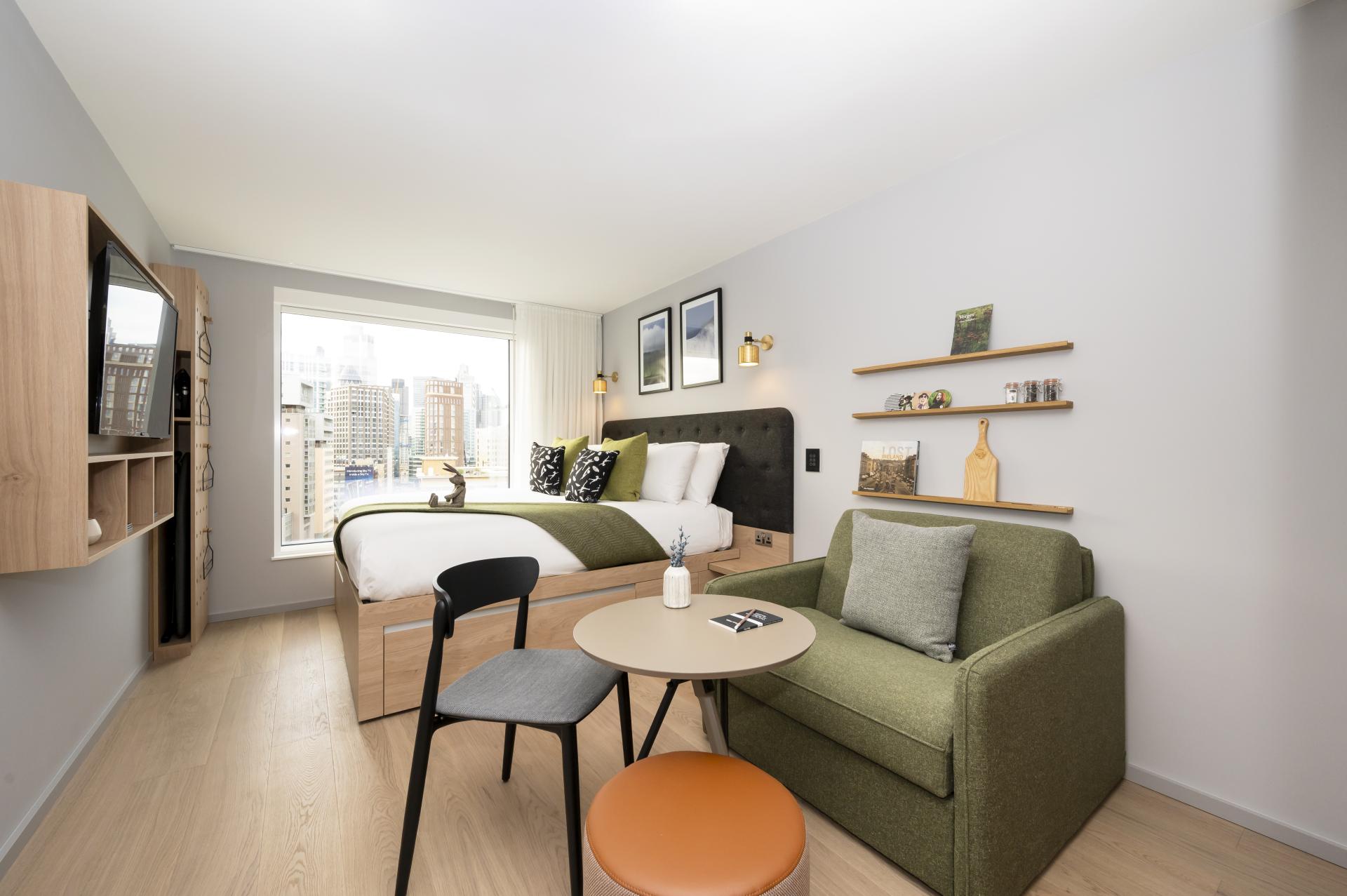 Modern hotel room featuring a green-themed decor, cozy seating area, and city skyline view, celebrating sustainable design.