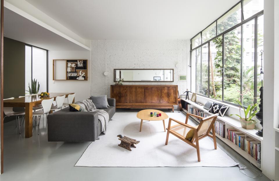 Renovated mid-century apartment interior with a cozy living area, wooden furniture, and large windows overlooking lush gardens.