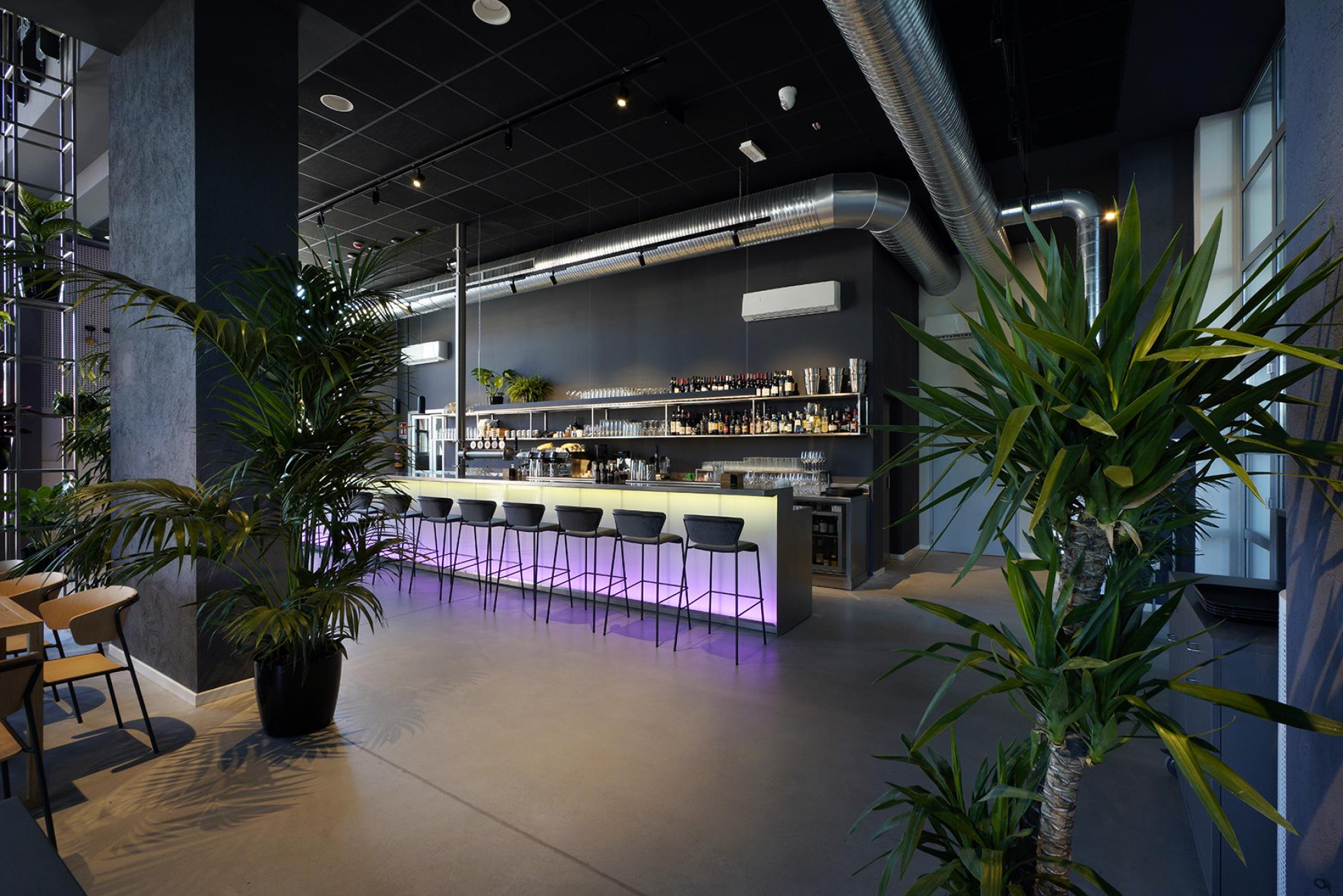 Modern bar interior featuring sleek design, vibrant lighting, and tropical plants, highlighting the cultural transformation of Bergamo’s former power plant.