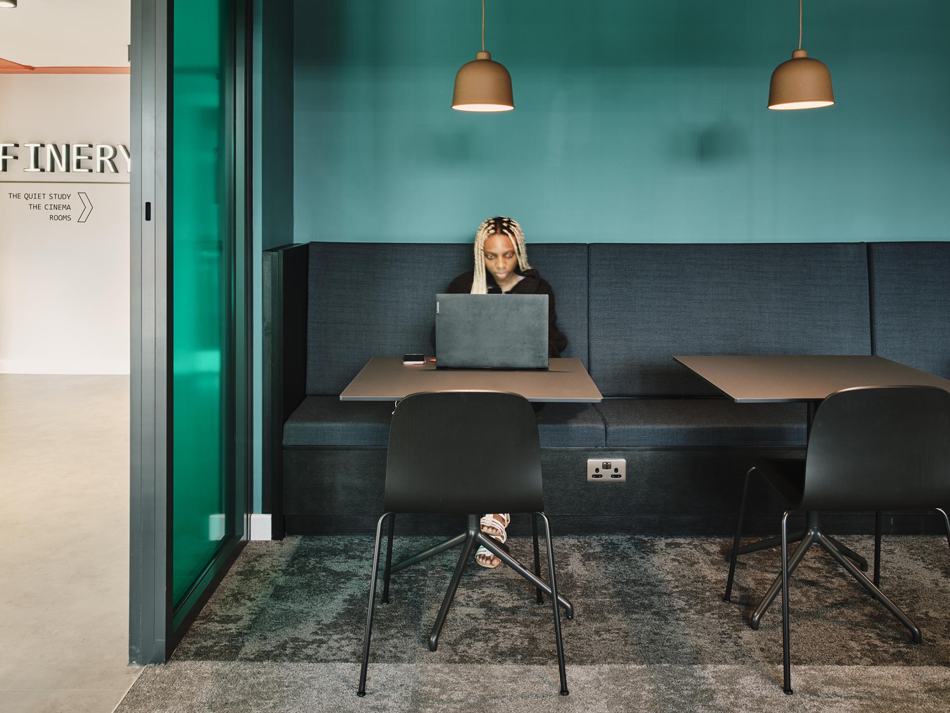 Modern study area in The Refinery student accommodation, featuring a student working on a laptop in a cozy nook.