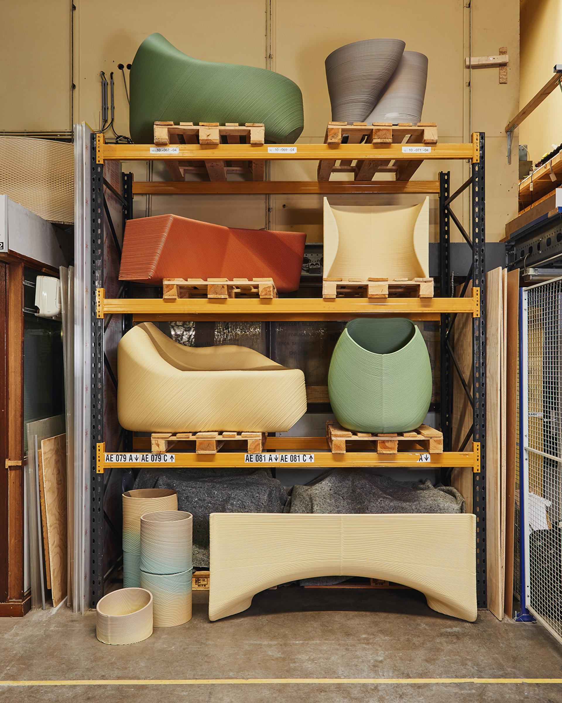 Colorful 3D-printed furniture pieces, including the Ermis chair, displayed on wooden pallets in a design studio setting.