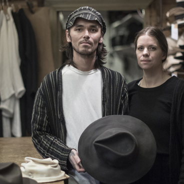 Craftspeople in Horisaki workshop showcasing handmade hats surrounded by a variety of traditional hat styles in Småland, Sweden.