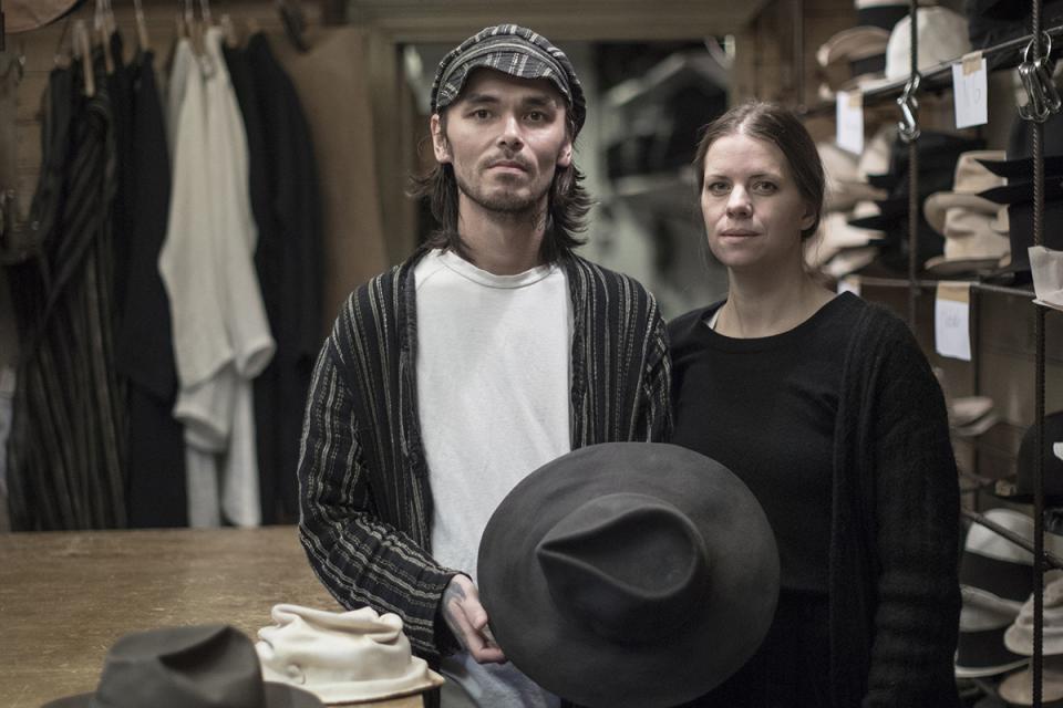 Craftspeople in Horisaki workshop showcasing handmade hats surrounded by a variety of traditional hat styles in Småland, Sweden.