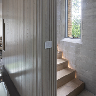 Modern interior with wooden stairs, textured walls, and natural light streaming through a large window, showcasing effective lighting design.