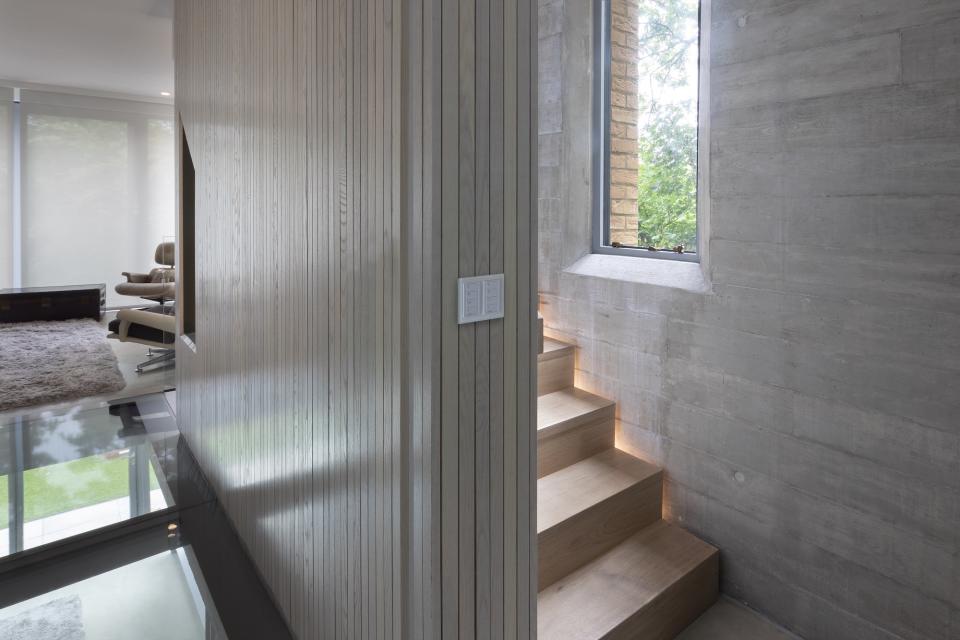 Modern interior with wooden stairs, textured walls, and natural light streaming through a large window, showcasing effective lighting design.