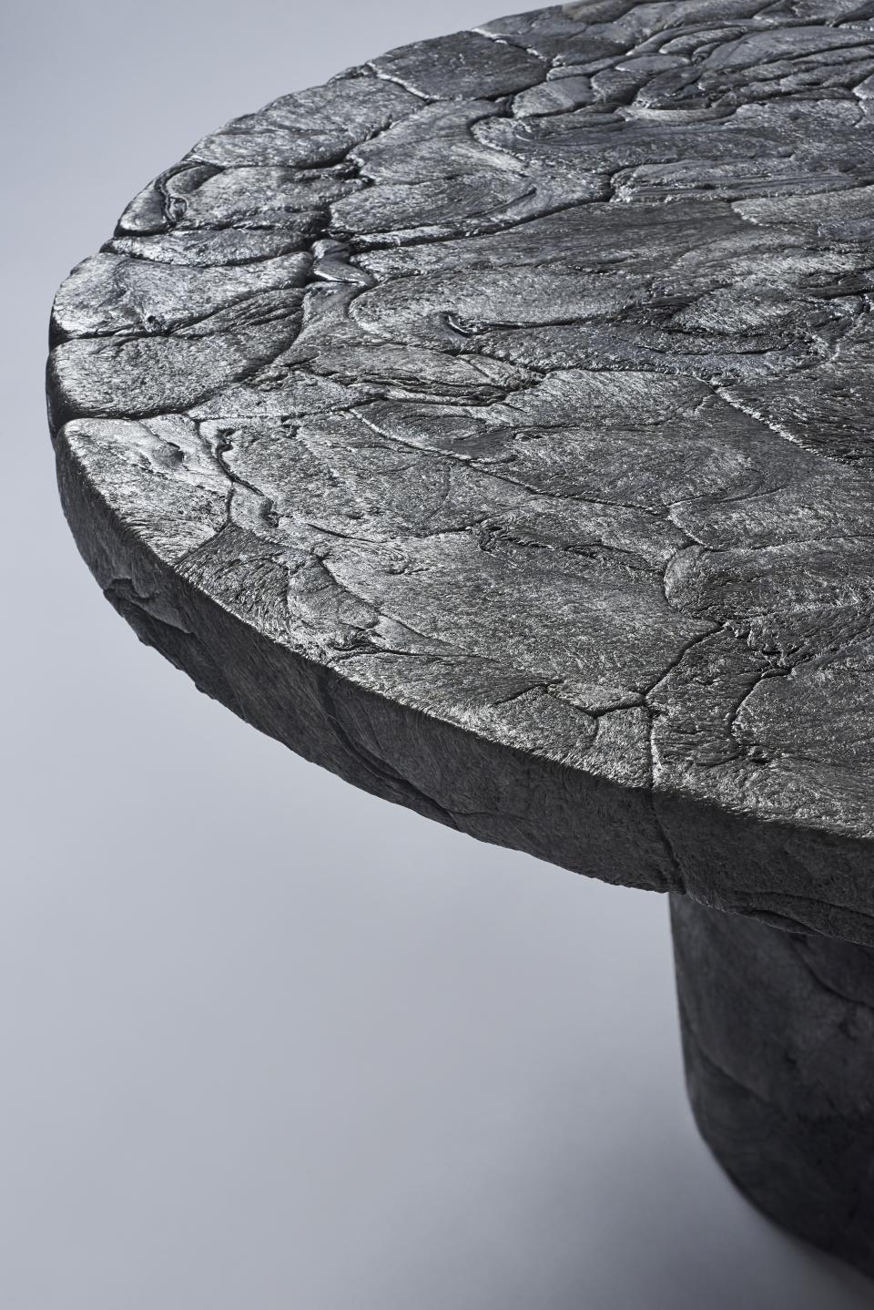 Sculptural table made from recycled styrofoam, showcasing a textured charcoal finish, reflecting innovative urban design principles.