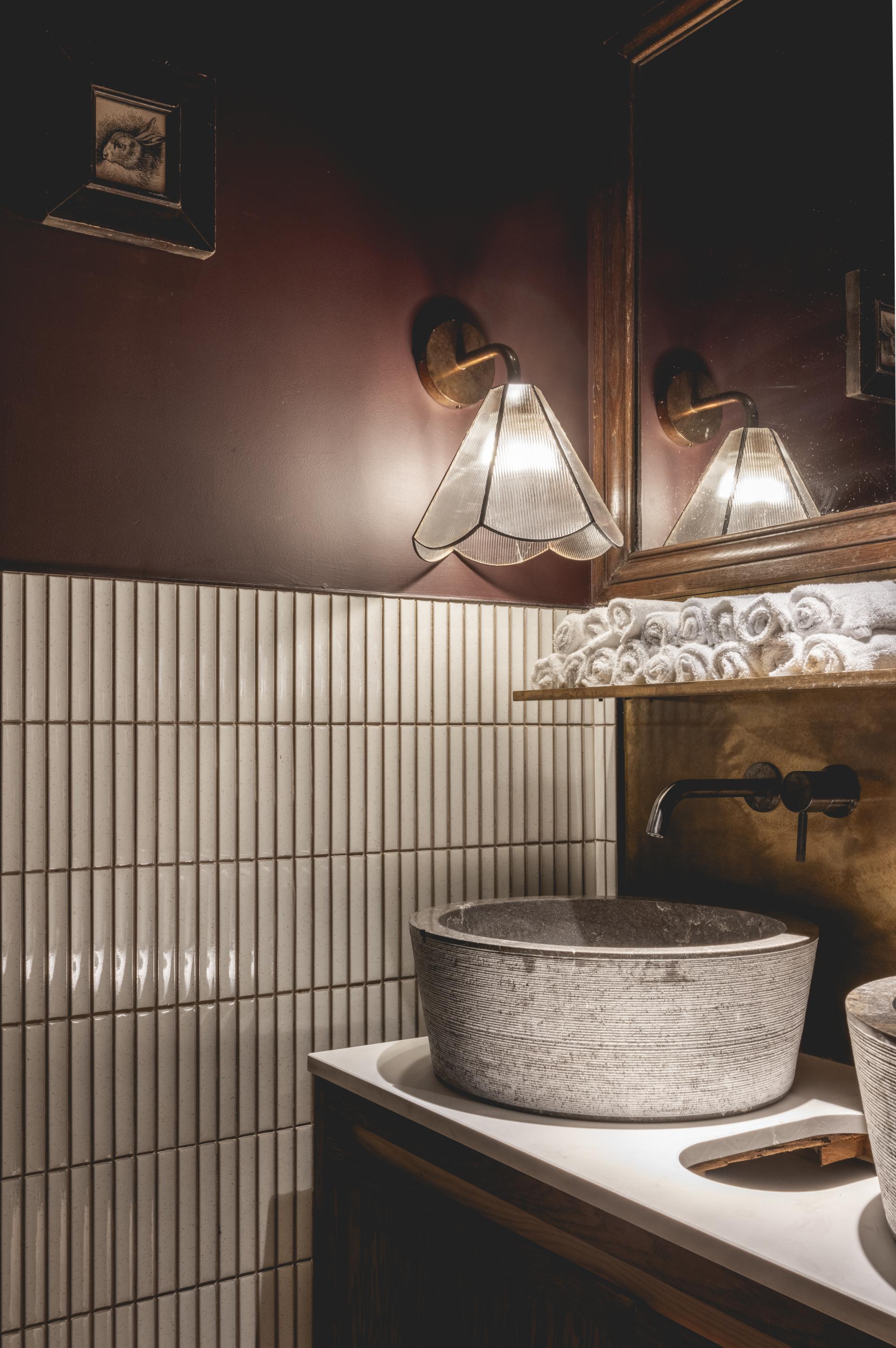 Elegant bathroom design features a rustic stone sink, vintage lighting, and textured wall tiles in Fitzrovia restaurant.