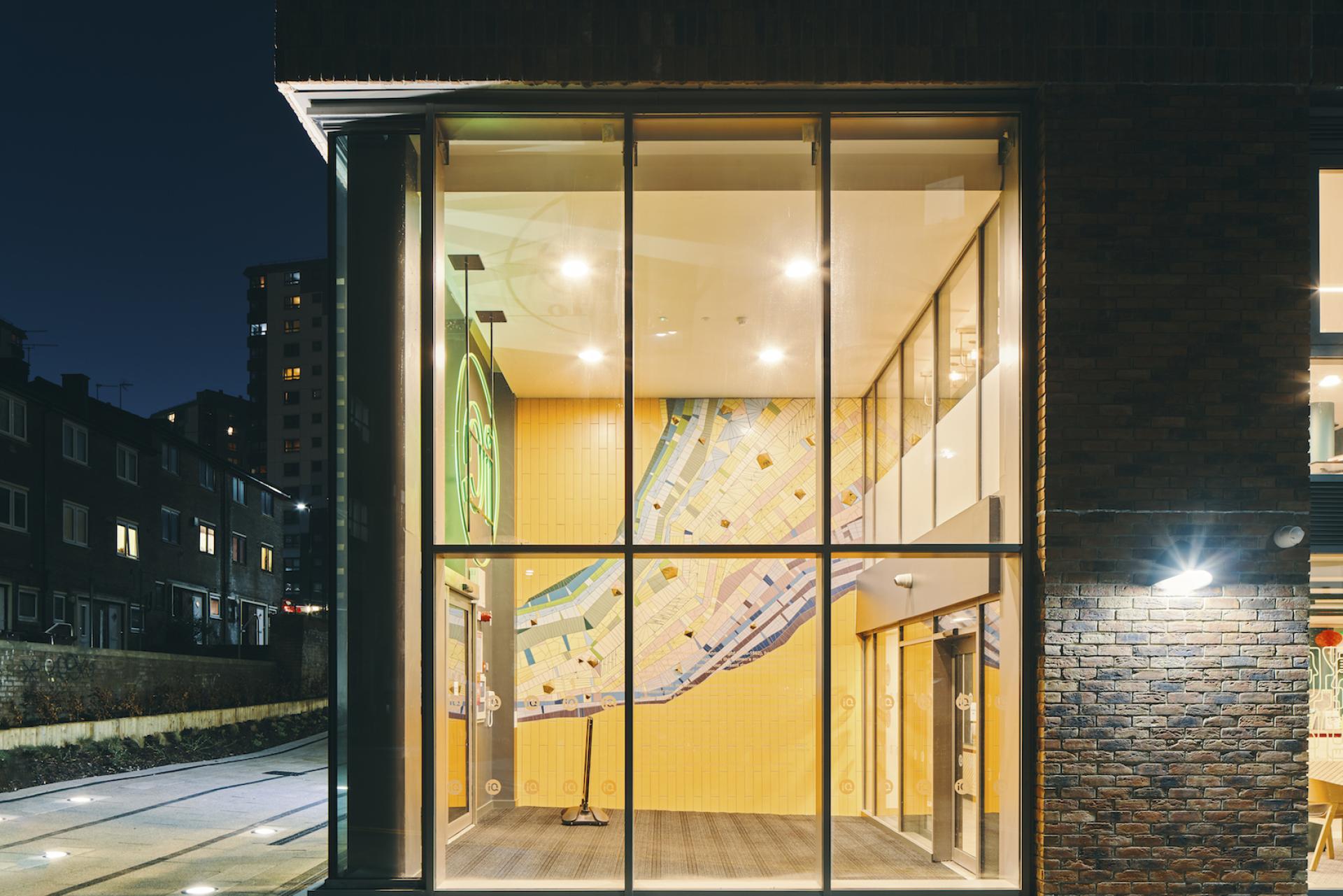 Knight House at the University of Sheffield features vibrant interiors and a striking yellow wall design, illuminated at night.