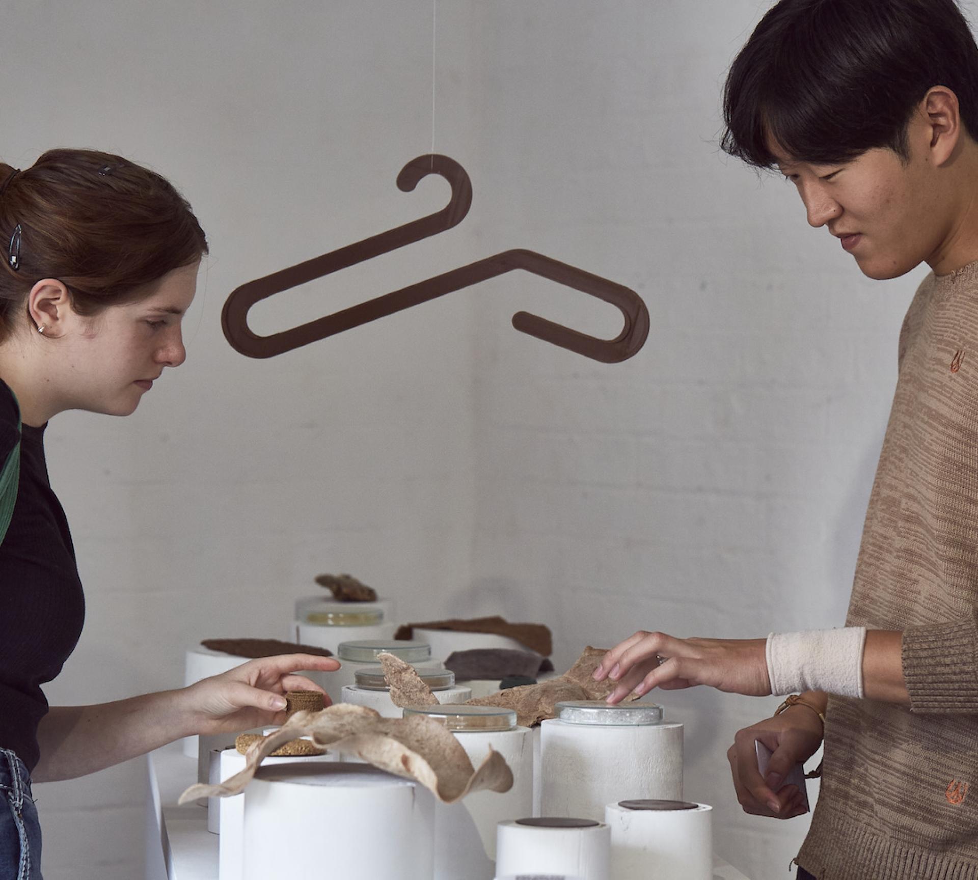 Two individuals examining sustainable biomaterials displayed on a table at a design exhibition, showcasing innovative material solutions.