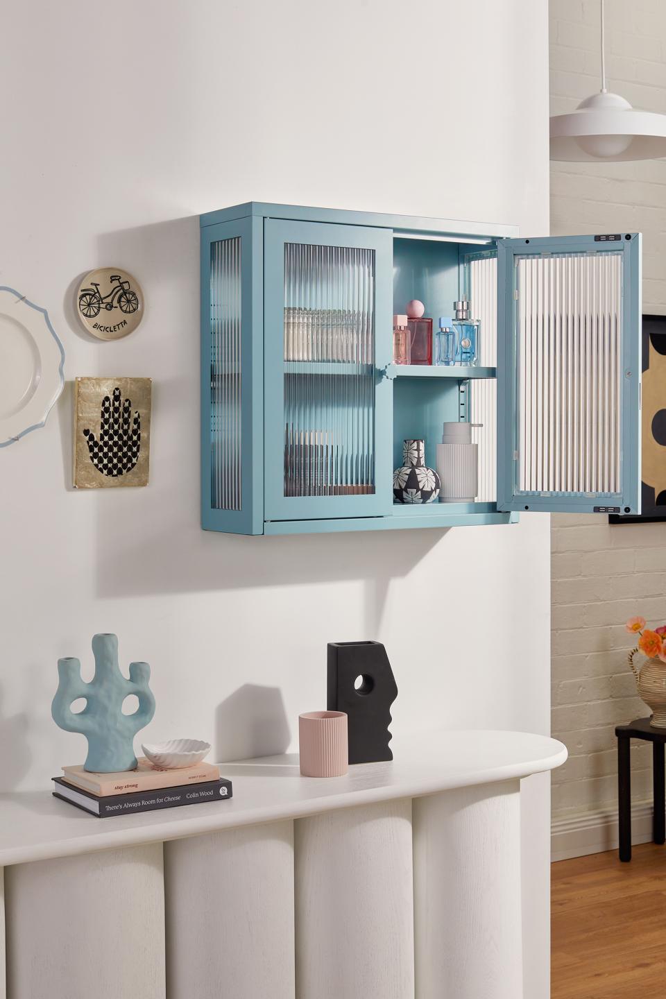 Stylish light blue cabinet showcasing The Glass Collection with decorative items on a white console table.
