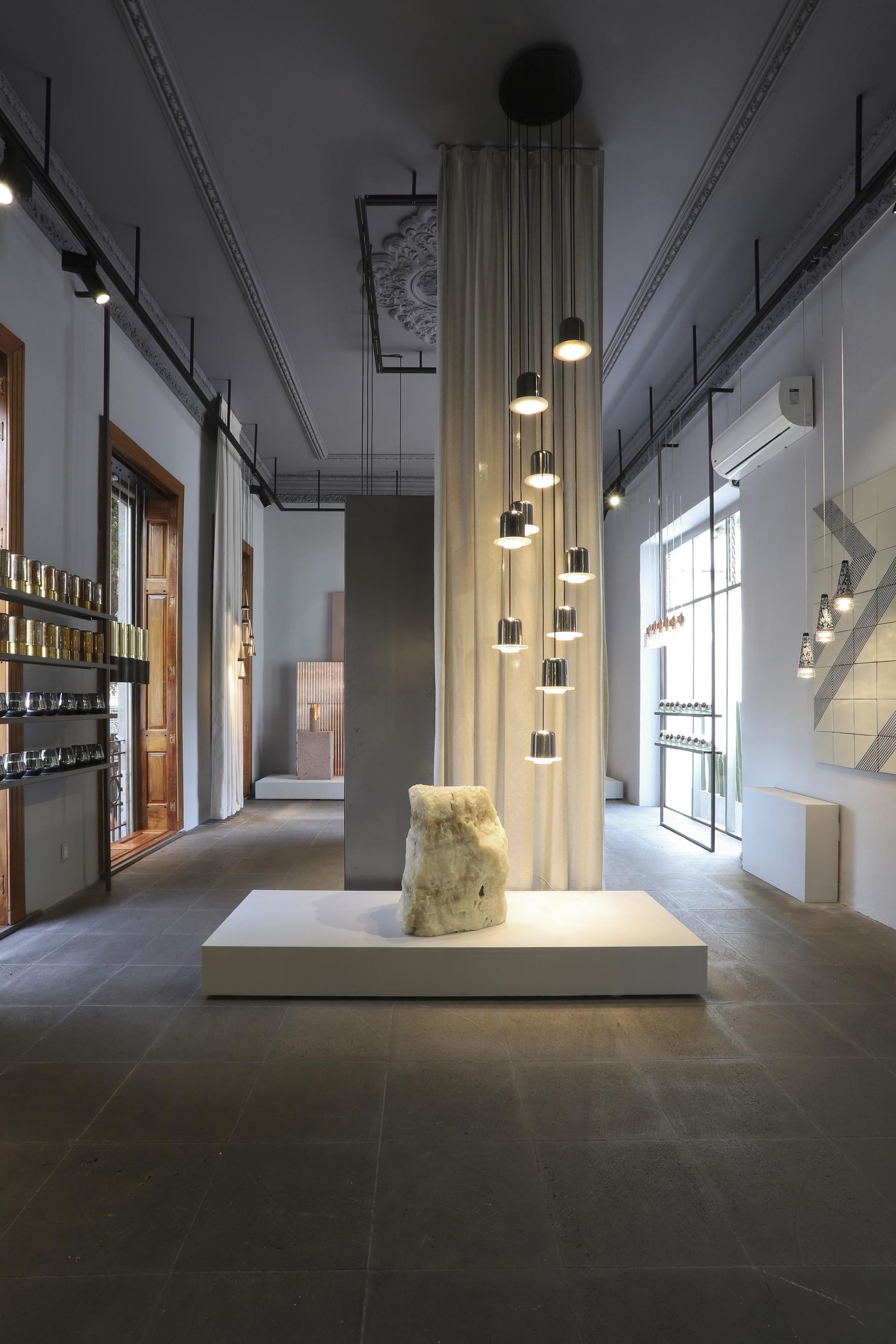 Showroom interior featuring local materials, suspended lighting fixtures, and a sculptural stone centerpiece in Mexico City.