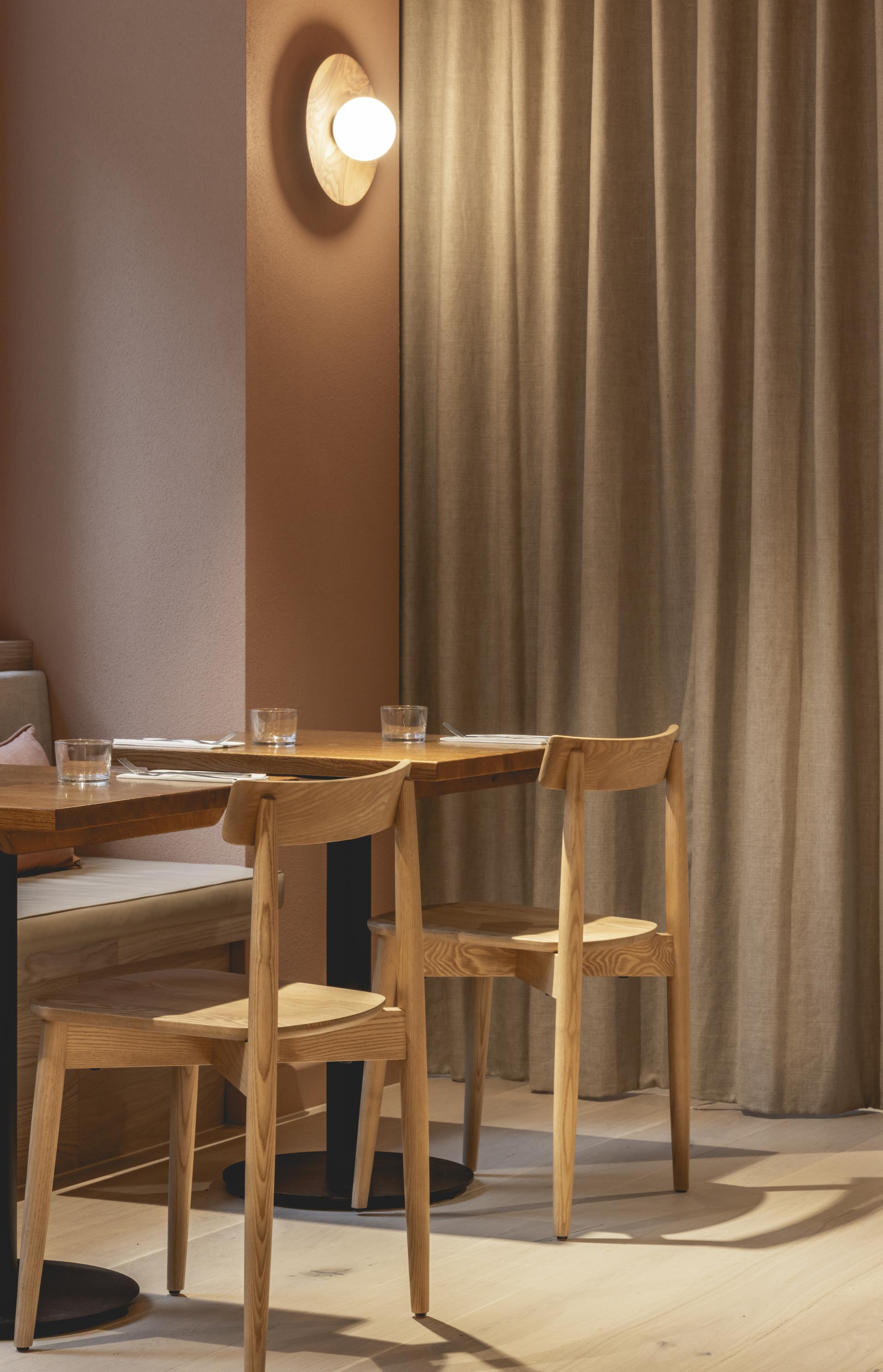 Warm-toned interior featuring wooden dining tables, minimalist chairs, and textured drapery at Honey & Co’s new deli.