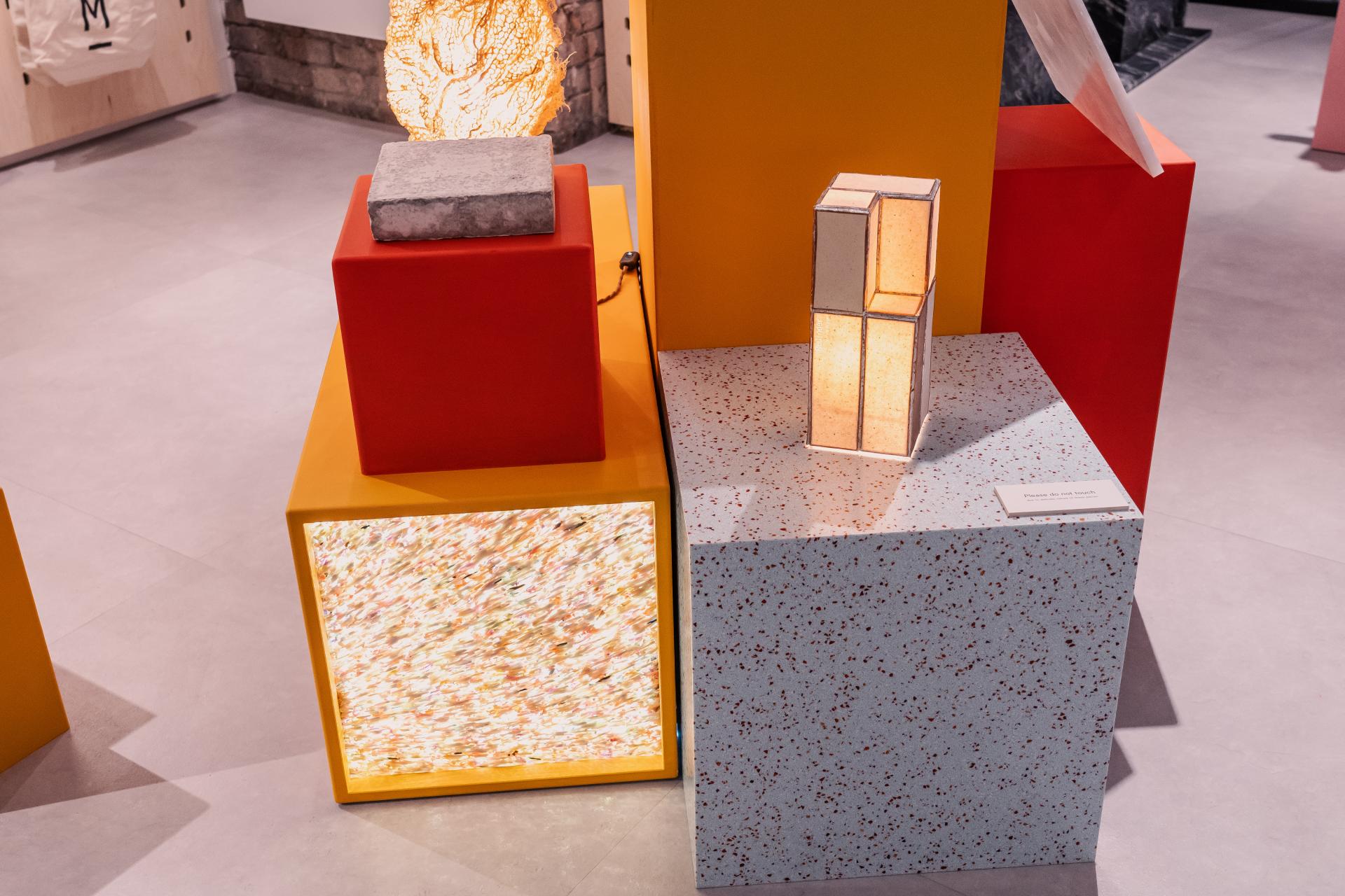 Colorful display showcasing sustainable design materials, including textured surfaces, illuminated elements, and stacked geometric forms.