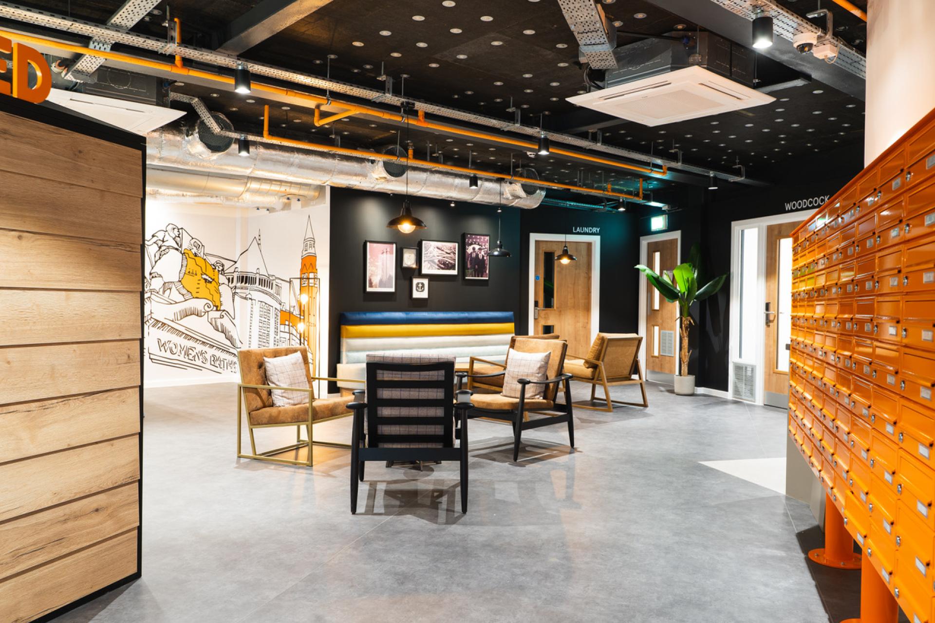 Modern student accommodation common area featuring stylish seating, vibrant wall art, and bright mailbox storage at Bath Court in Birmingham.
