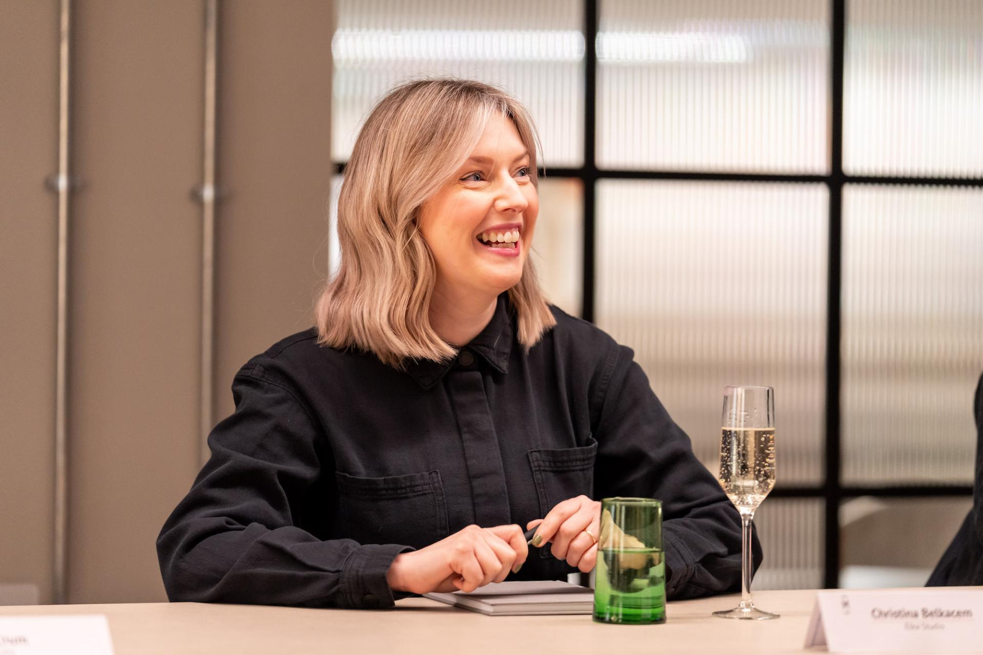 Engaged participant smiling during a roundtable discussion on sustainability and value engineering, with drinks on the table.