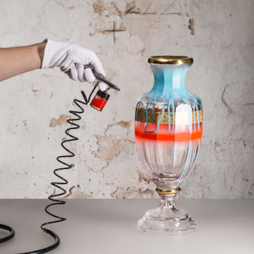 Artist applying vibrant colors to a decorative glass vase, showcasing innovative glass art techniques at the London Design Fair.