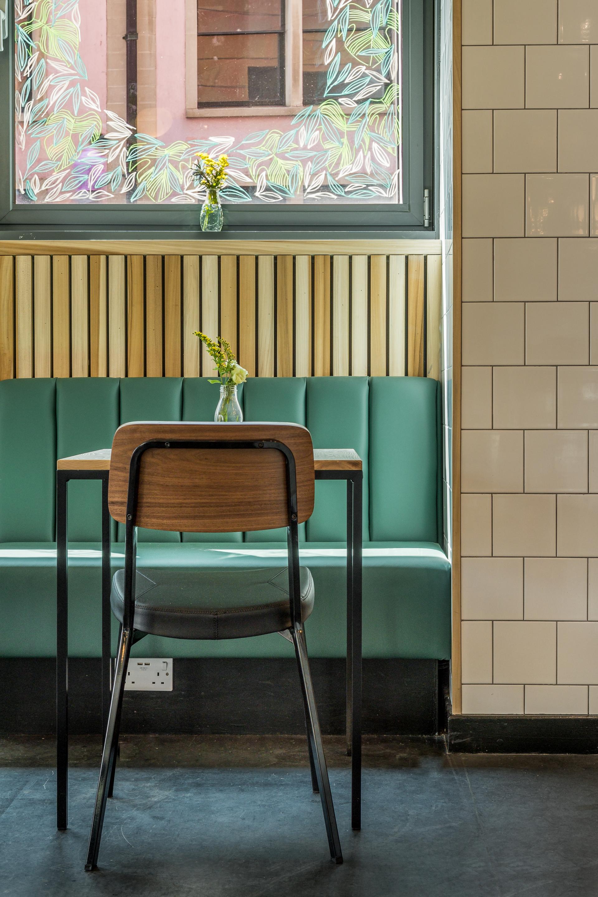 Cozy café interior of Bristol Loaf featuring a green banquette, wooden table, and floral vase by the window.