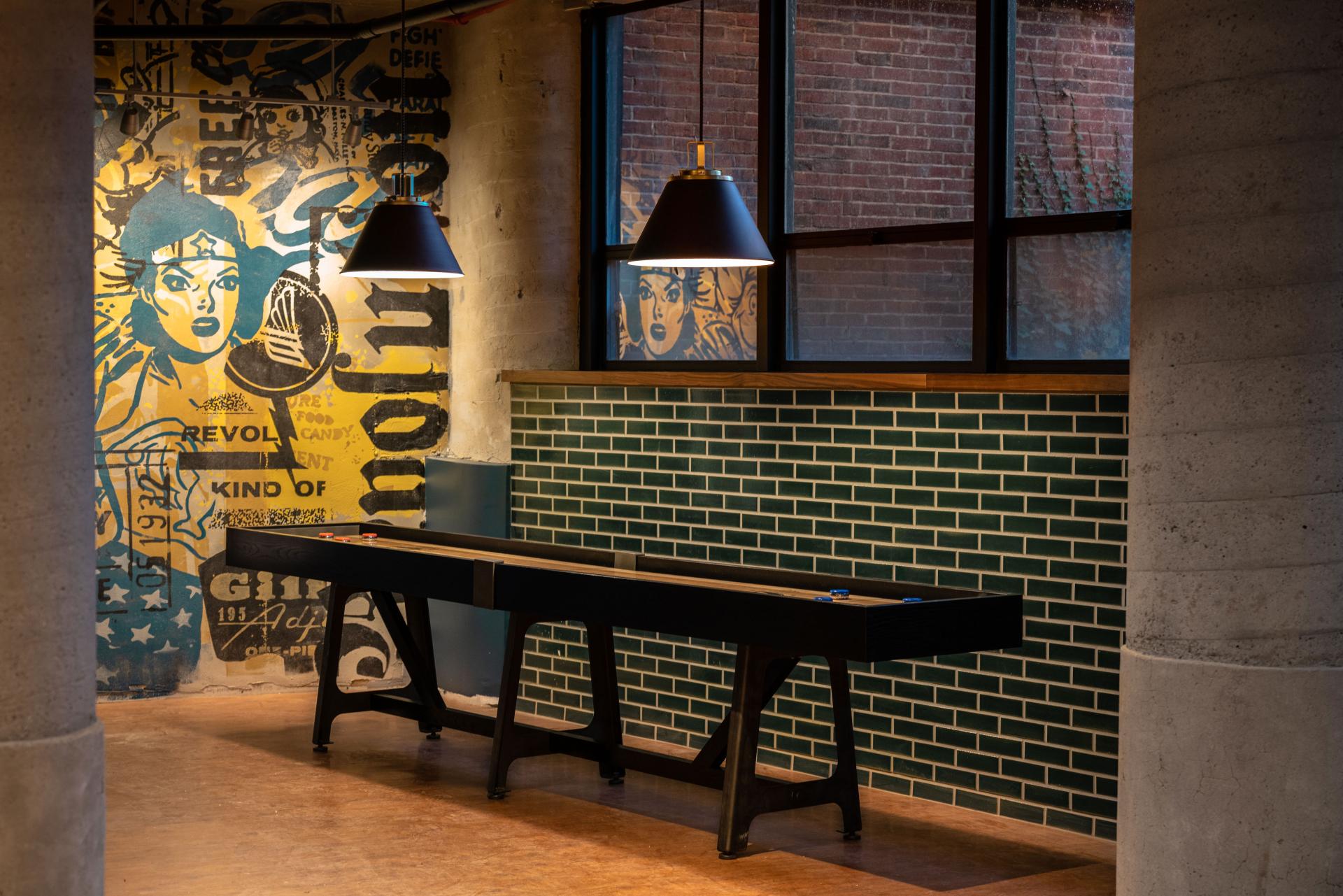 Modern interior design of The Revolution Hotel in Boston featuring a shuffleboard, vintage mural, and green tile accents.