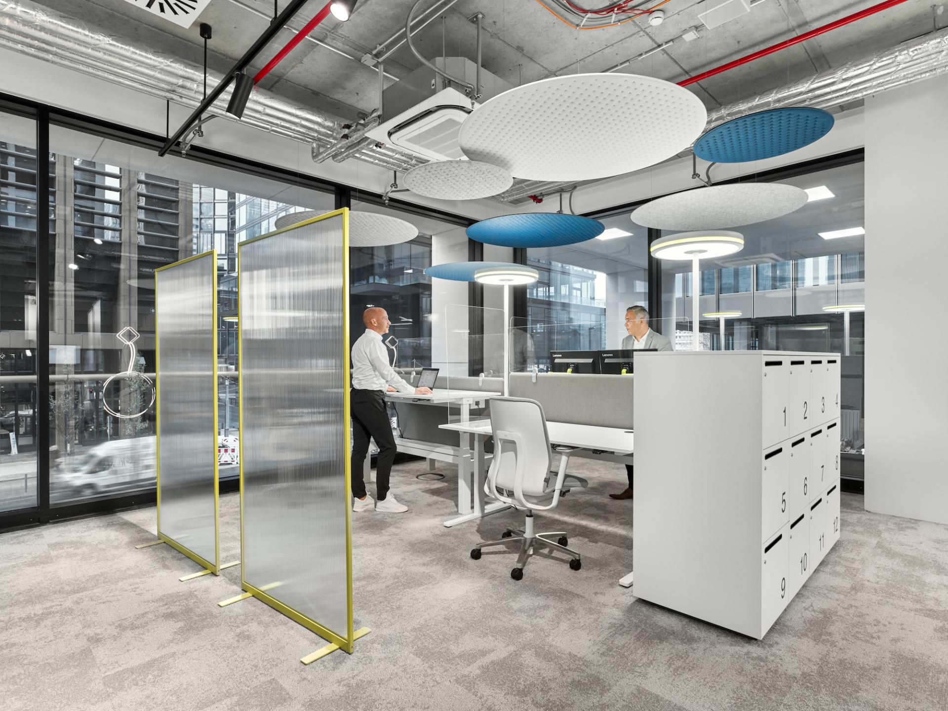 Modern office space with transparent partitions, ergonomic furniture, and vibrant acoustic panels, designed for post-pandemic workplace functionality.
