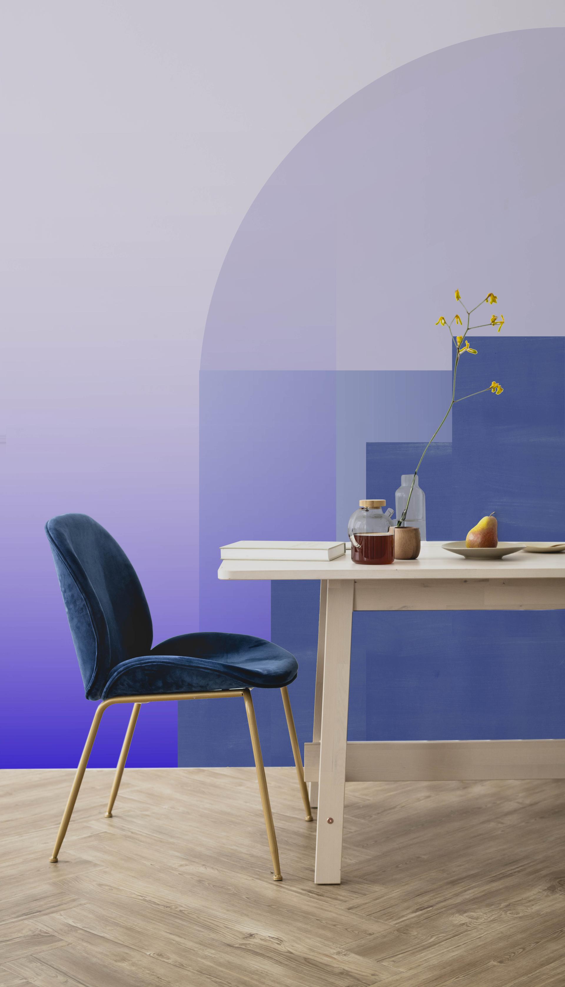 Modern workspace featuring a stylish blue velvet chair beside a wooden table, adorned with decorative items and a colorful wall.