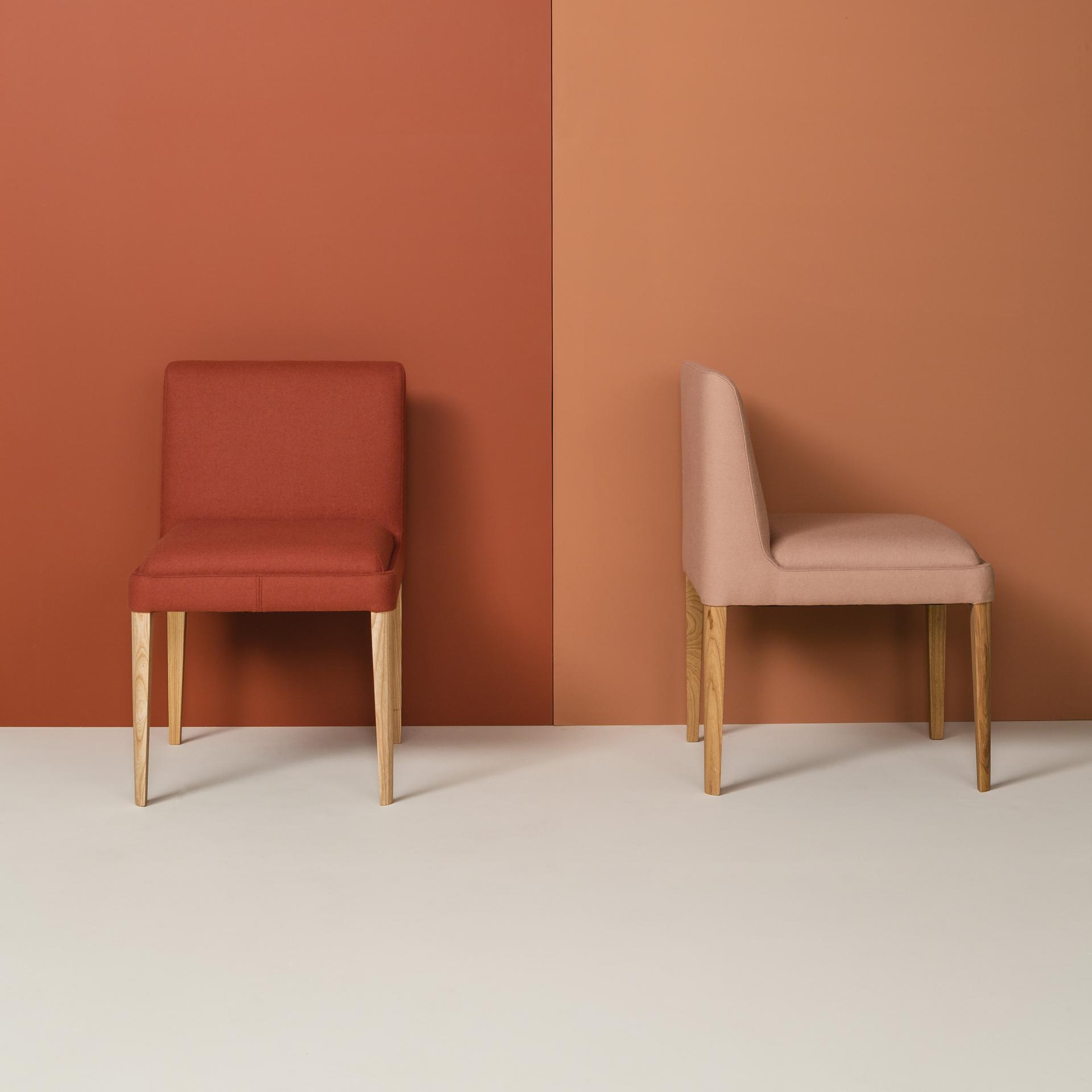 Two stylish chairs from the Kyoto collection, featuring vibrant upholstery and natural wood legs against a warm, minimalist background.
