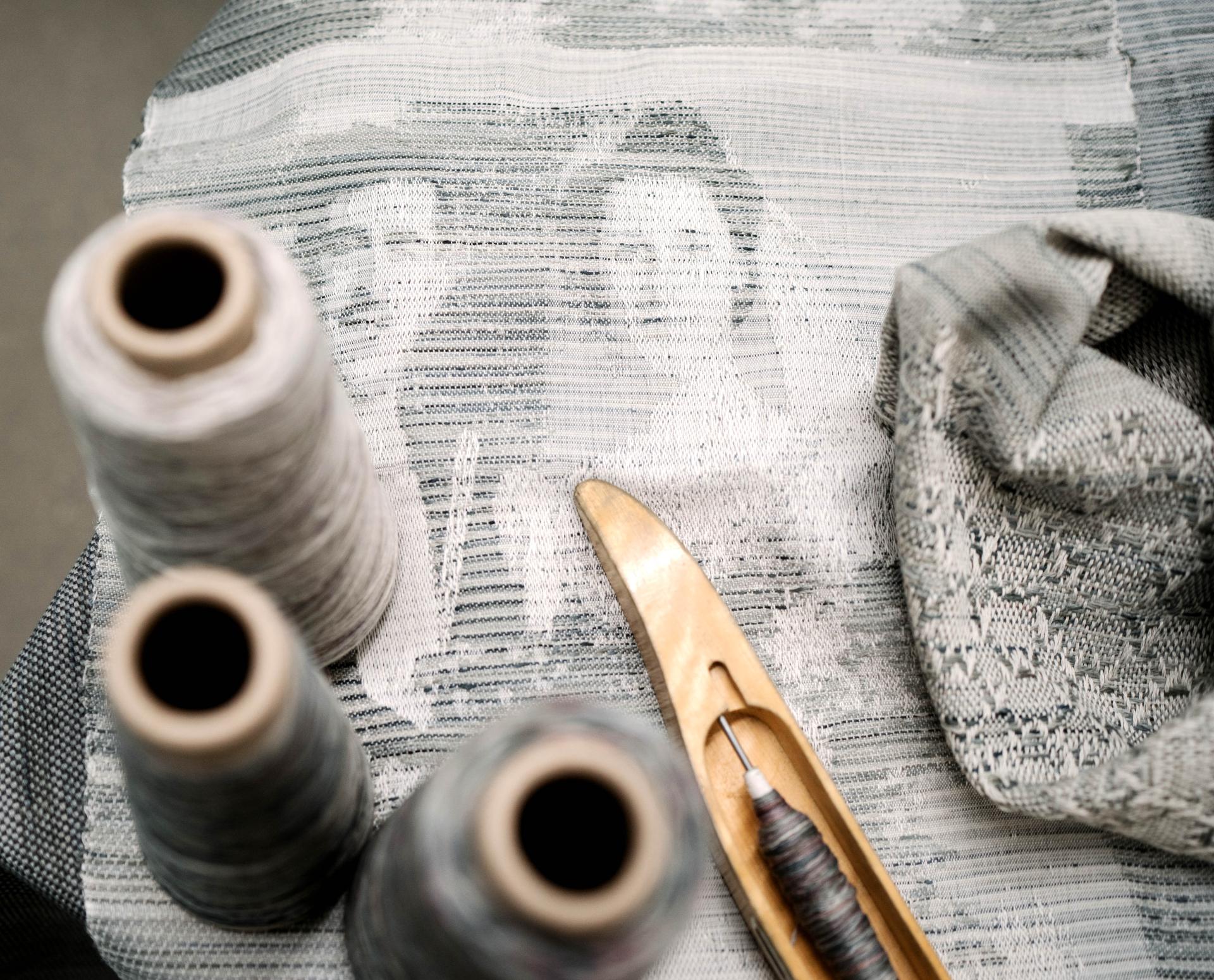 Textile art showcasing intricate pattern weaving with spools of thread and weaving tools, highlighting designer creativity at New Designers 2022.