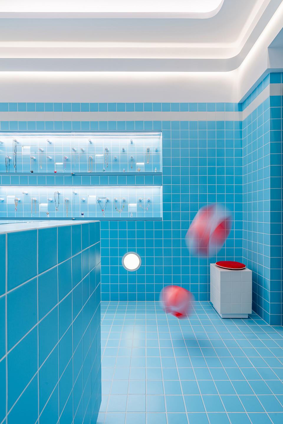 Bright blue-tiled jewellery shop interior inspired by Wes Anderson, featuring elegant displays and playful red objects.