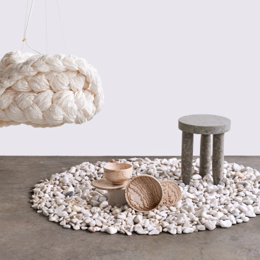 Textured stone setting featuring a unique hanging light, minimalist table, and handcrafted bowls in an innovative design display.