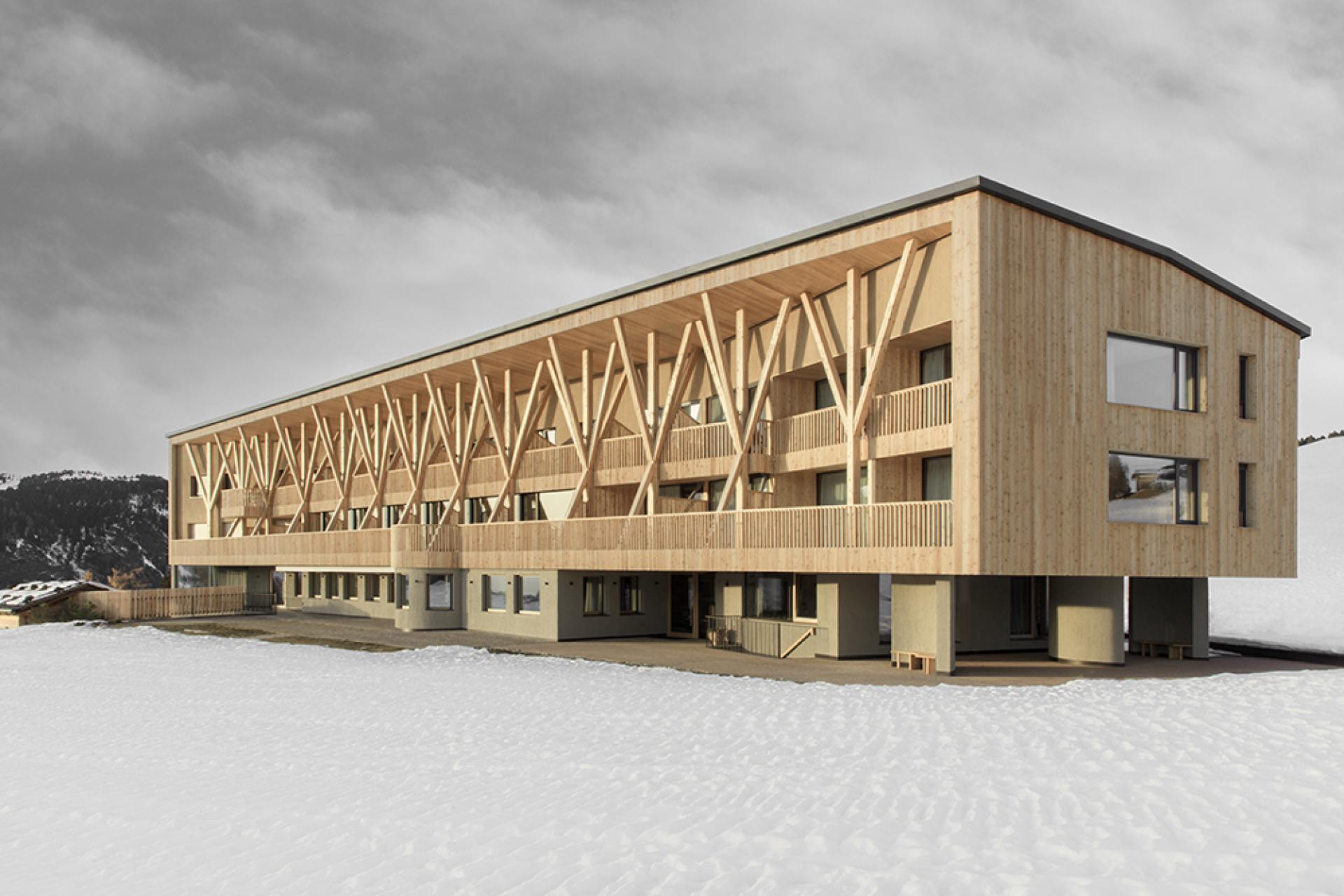 Modern wooden hotel with colonnades, set against the snowy Dolomite Mountains, showcasing alpine architecture and design.