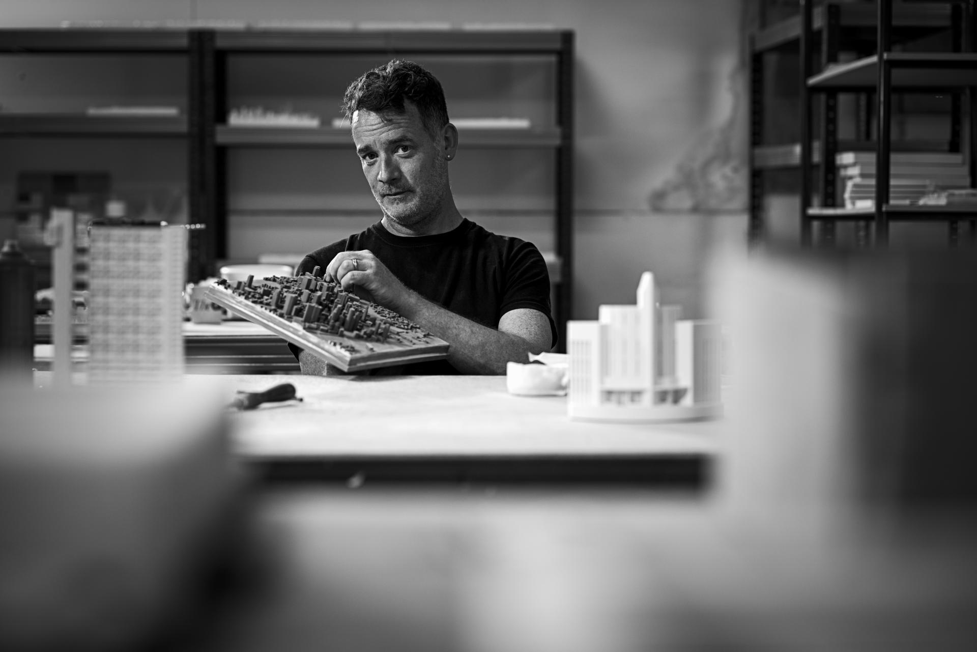 Designer showcasing a detailed architectural model in a studio, representing urban landscape creation with Chisel & Mouse.