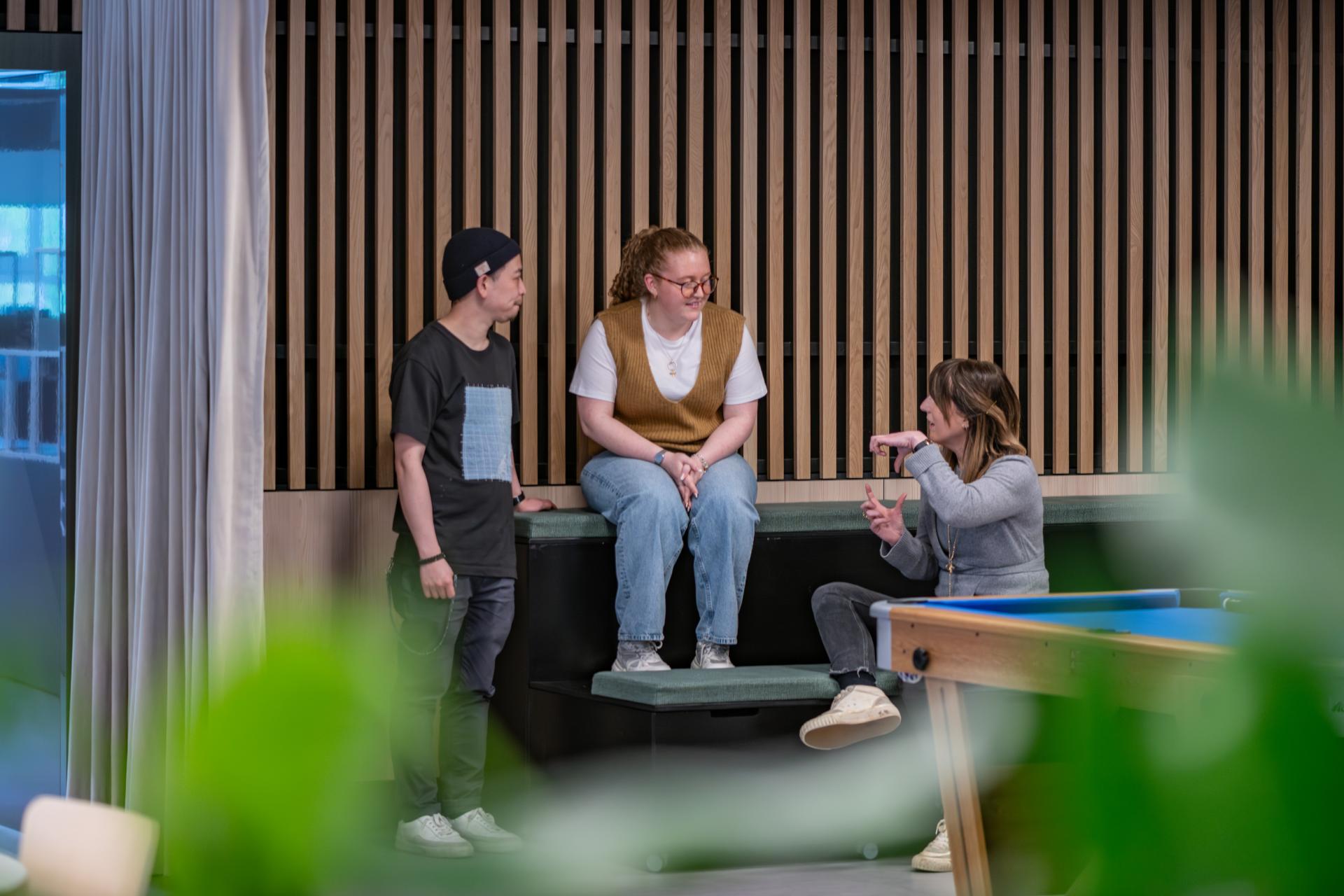 Three colleagues engage in conversation in a modern workspace designed for collaboration at a FinTech firm.