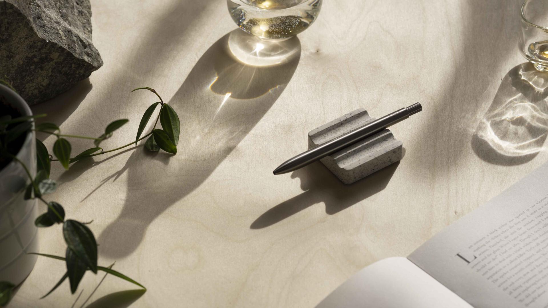 Stylish pen resting on ebonite terrazzo desk rest, surrounded by plants and glassware, showcasing AJOTO's innovative design.