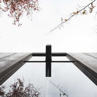 View from below of St Catherine’s College’s modern architecture reflecting autumn leaves and a cloudy sky.