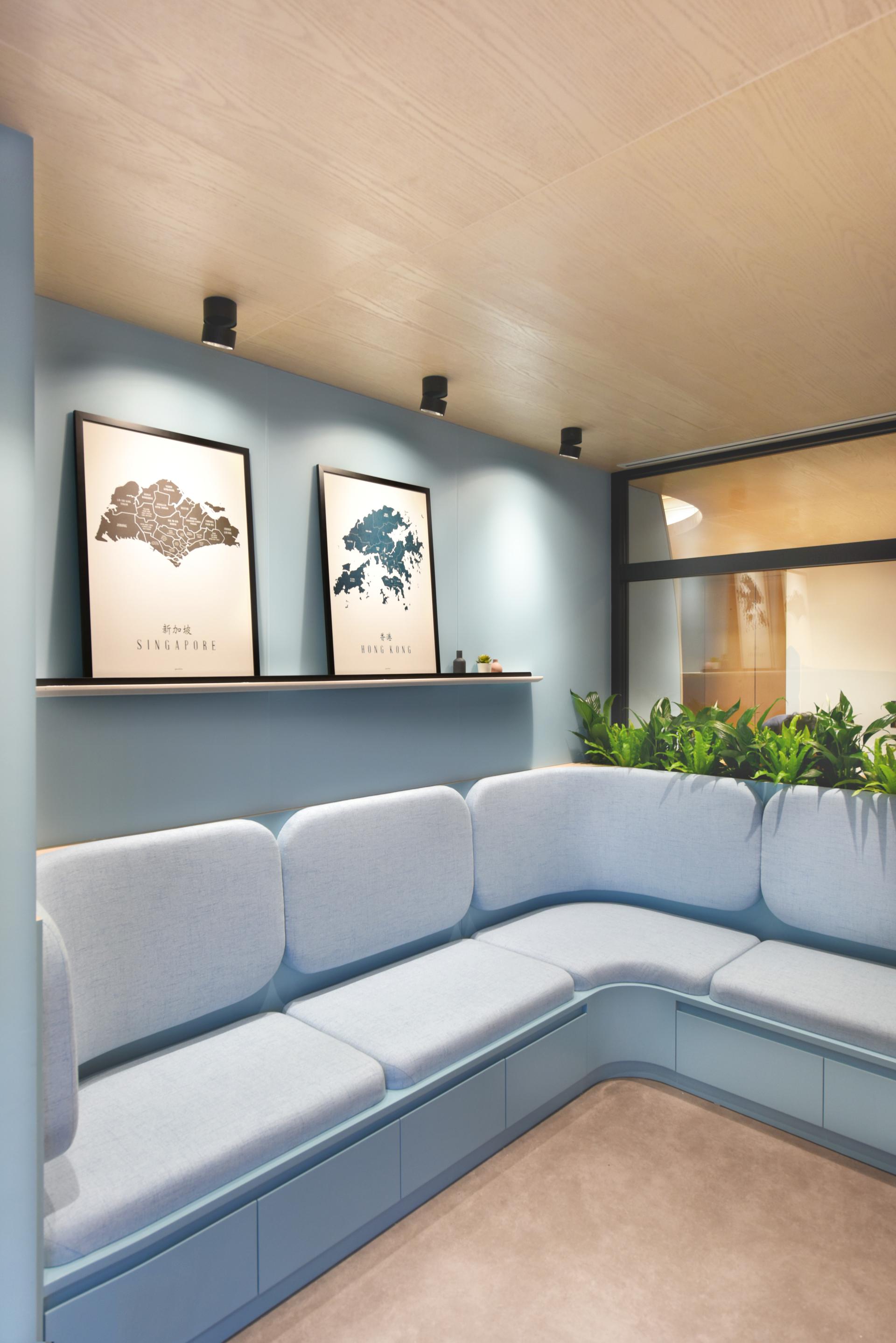 Modern office lounge featuring comfortable blue seating and framed maps of Singapore and Hong Kong, enhancing travel tech design.