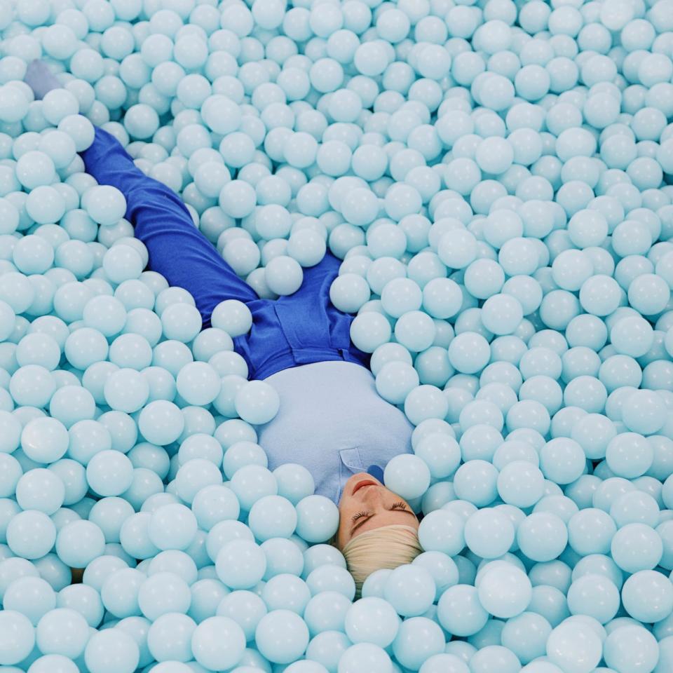 A person lying in a pool of pastel blue plastic balls at the vibrant Color Factory exhibition in New York City.