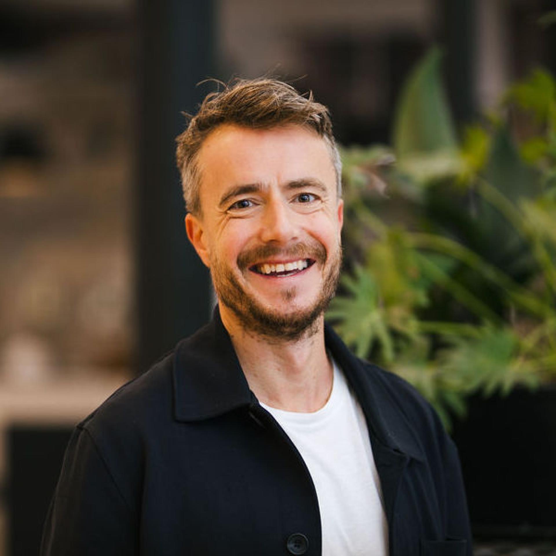 Smiling man in casual attire against a backdrop of greenery, discussing Glasgow's property outlook and future trends.