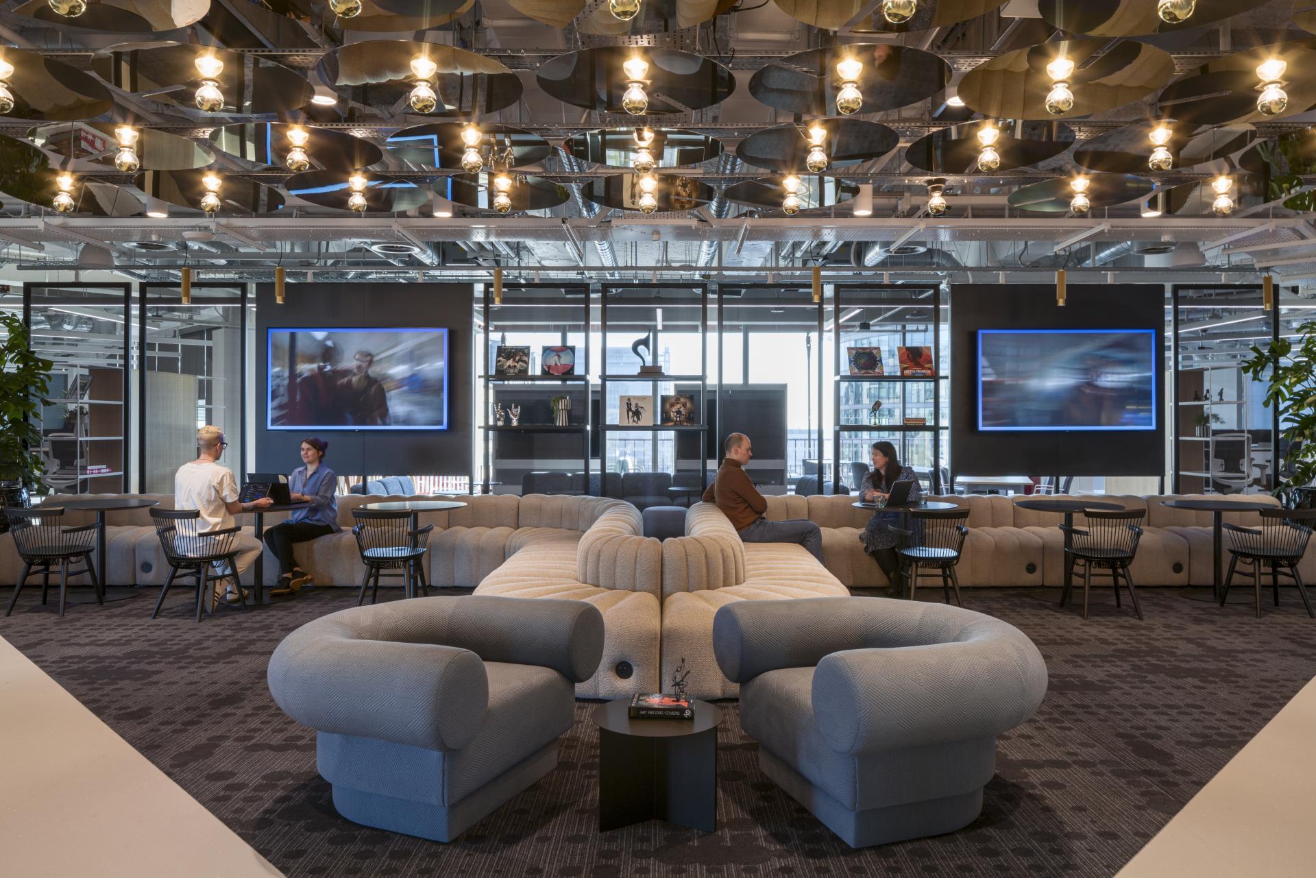 Modern office lounge area at Virgin Media O2 headquarters featuring collaborative seating, large screens, and vibrant decor.