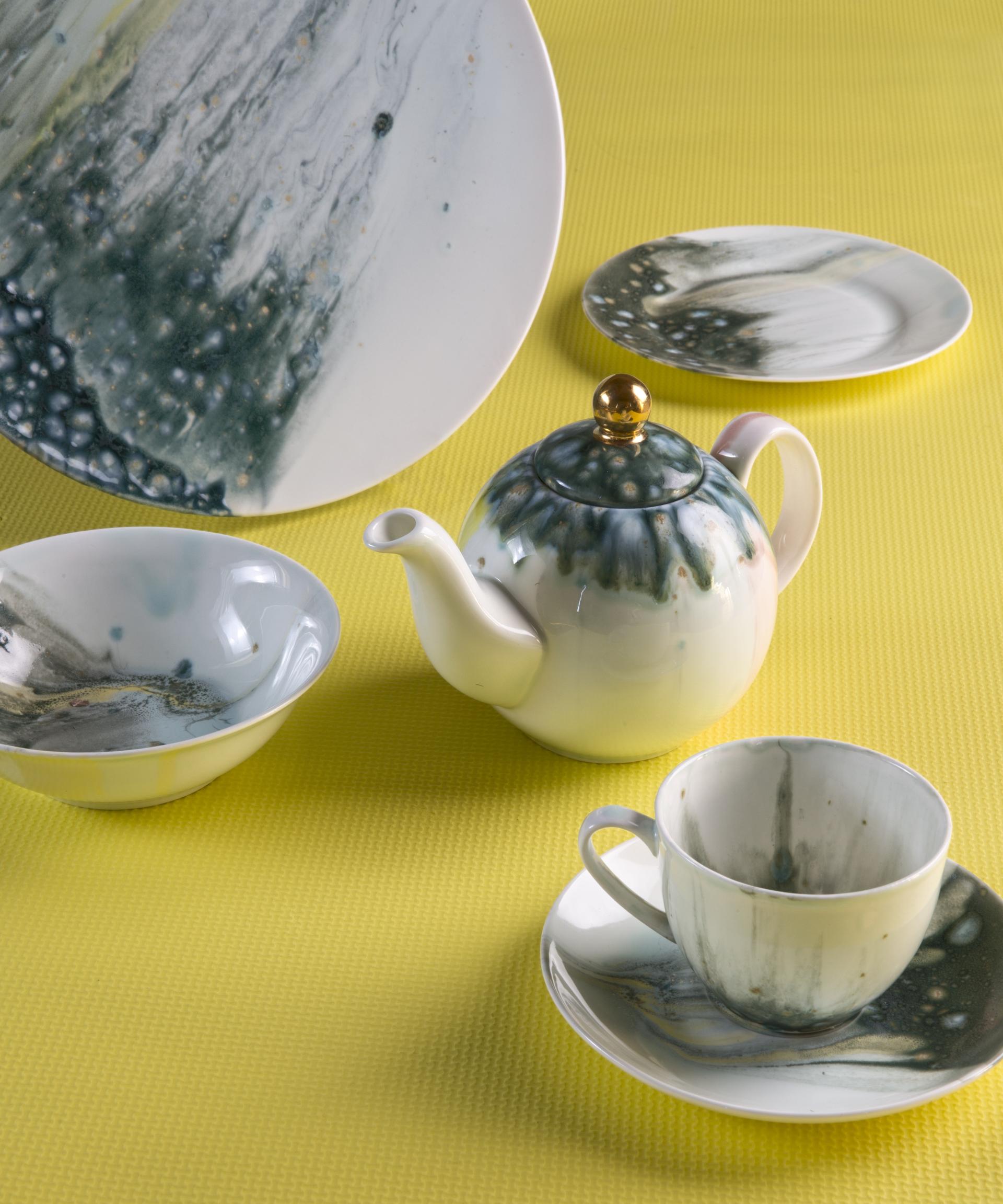 Ceramic tea set with a teapot, teacup, and plates featuring a unique green and blue marbling design on a yellow background.